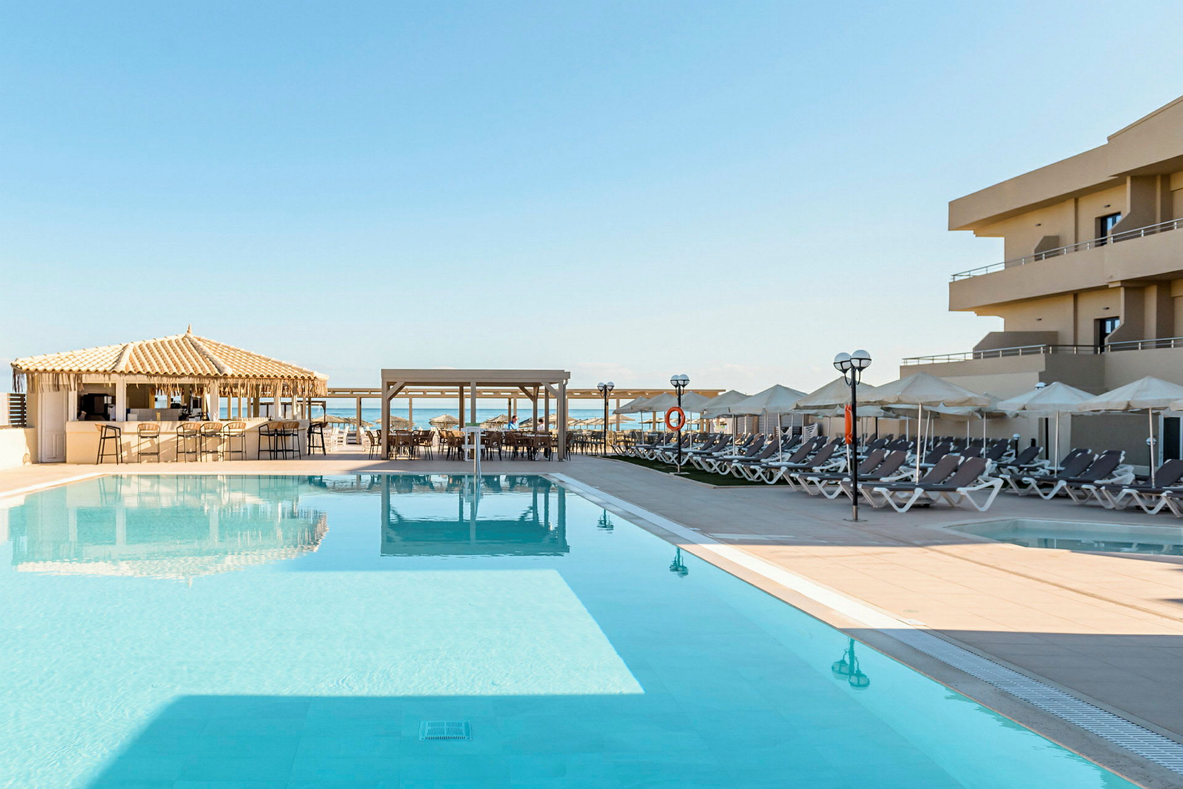 Bild av ett hotellområde med en stor pool, solstolar och parasoller samt en bar nära poolen. (AI-genererad text)