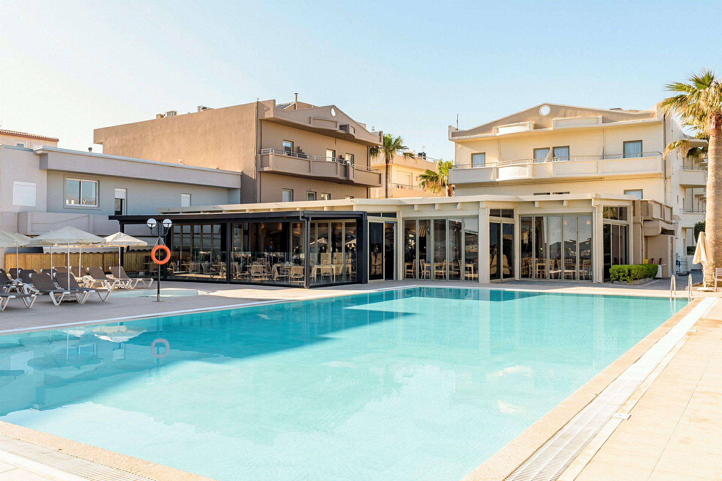 Utomhuspool med sittplatser och parasoller i anslutning till hotellbyggnader. (AI-genererad text)