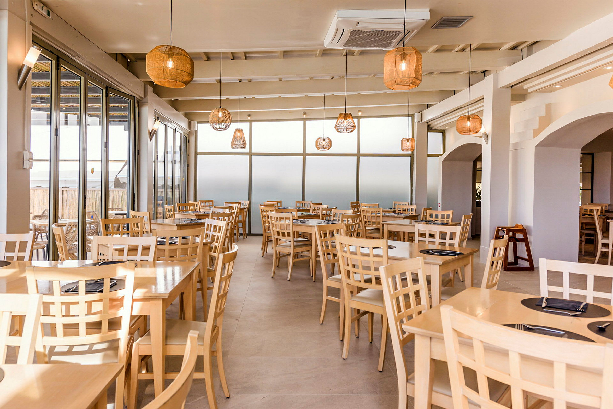 En restaurang med träbord och stolar, stora fönster och hängande lampor. (AI-genererad text)