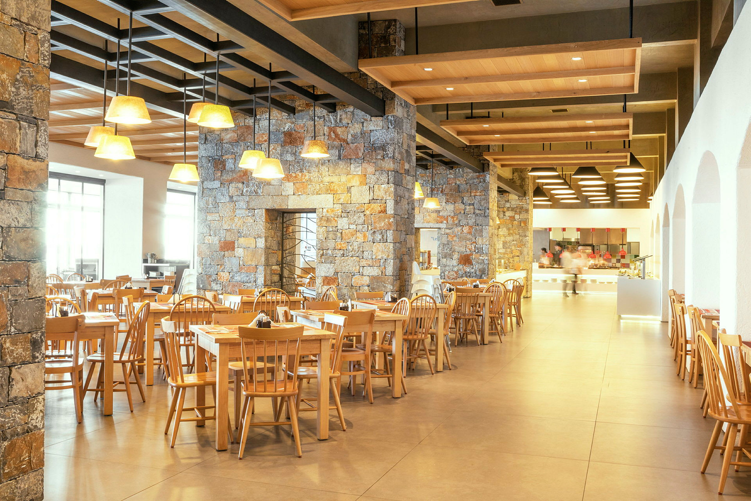 Restaurang med trästolar och bord samt stenväggar och taklampor. (AI-genererad text)