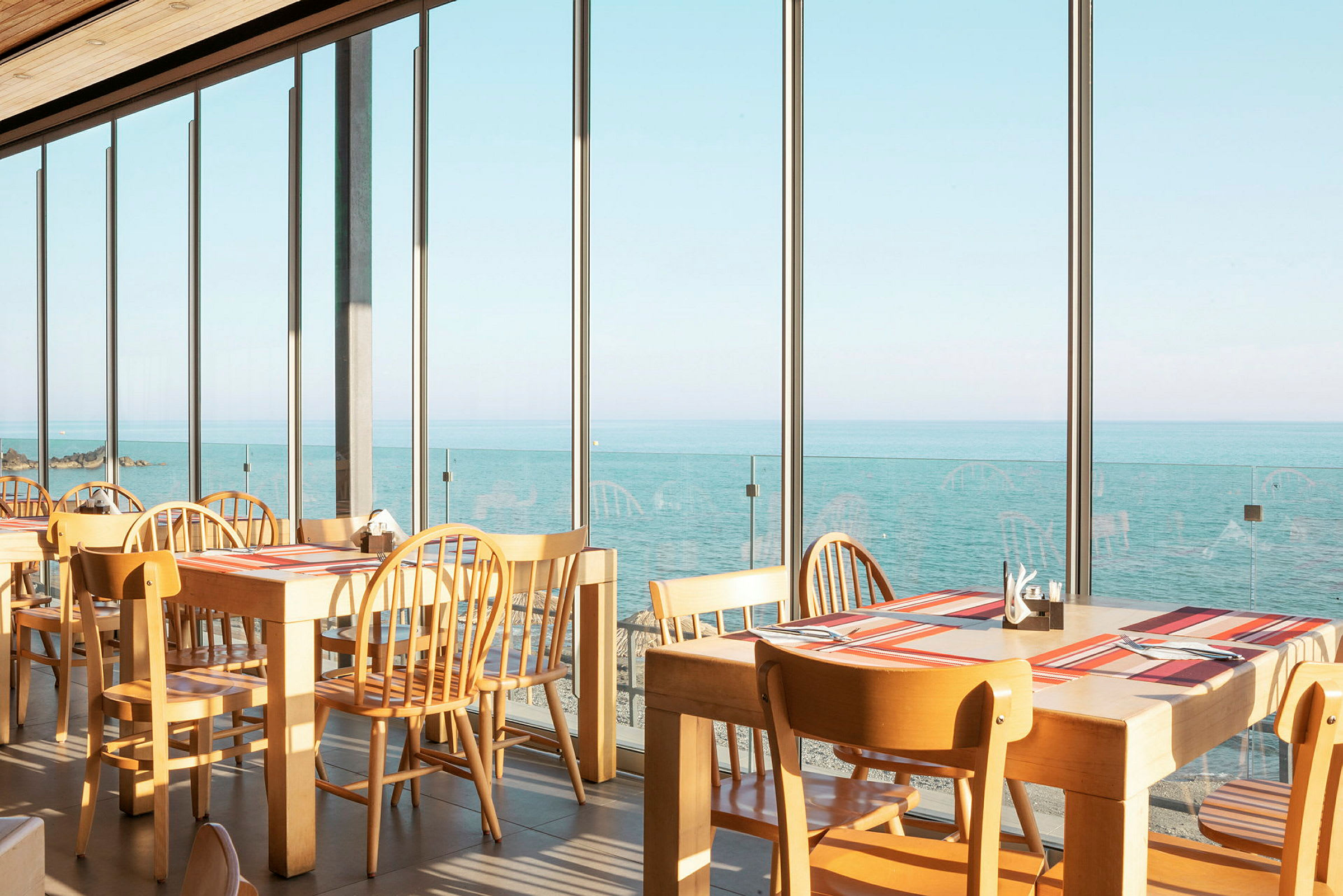 Restaurang med bord och stolar vid stora fönster som vetter mot havet. (AI-genererad text)