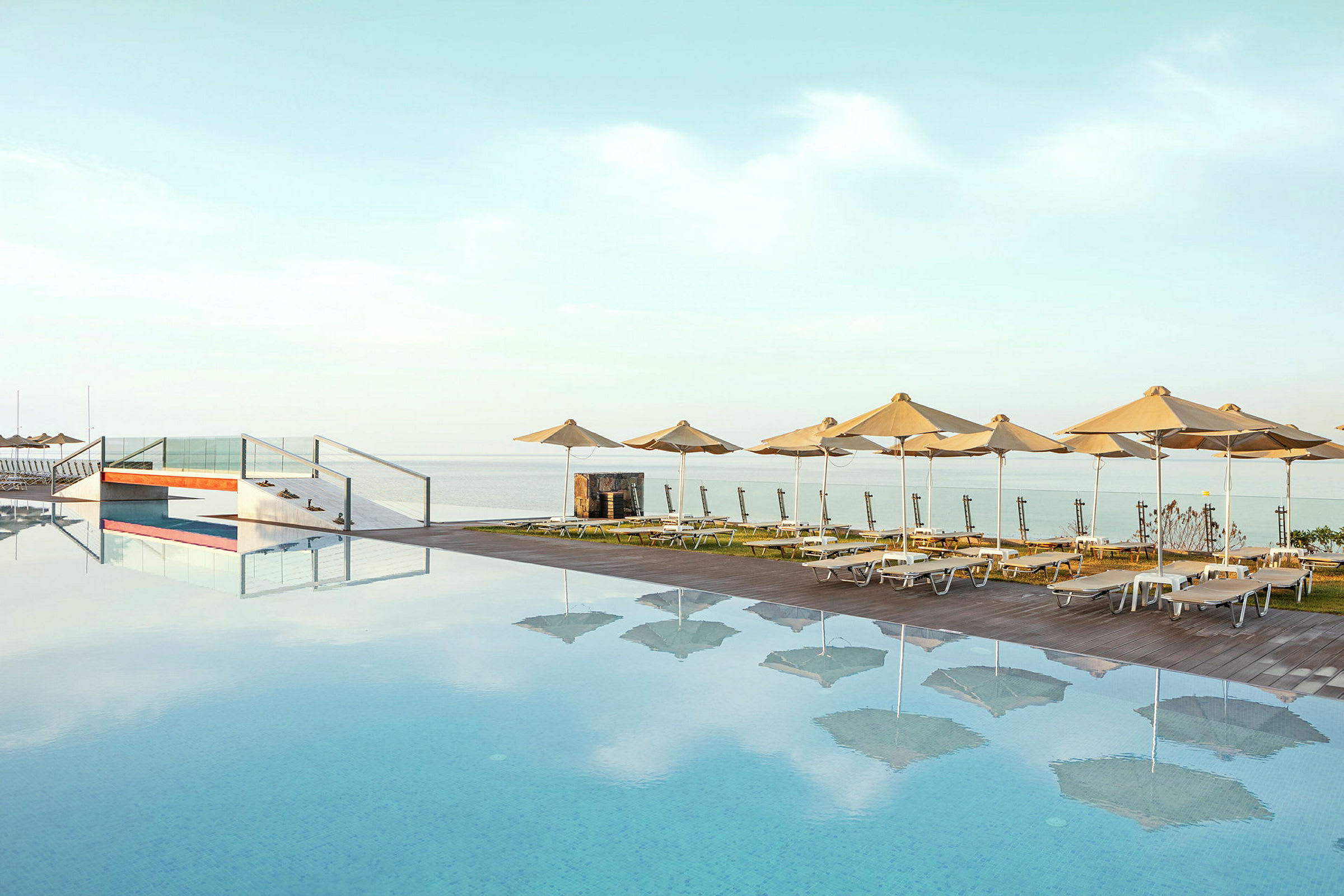 En infinitypool med solstolar och parasoller vid kanten med havet i bakgrunden. (AI-genererad text)
