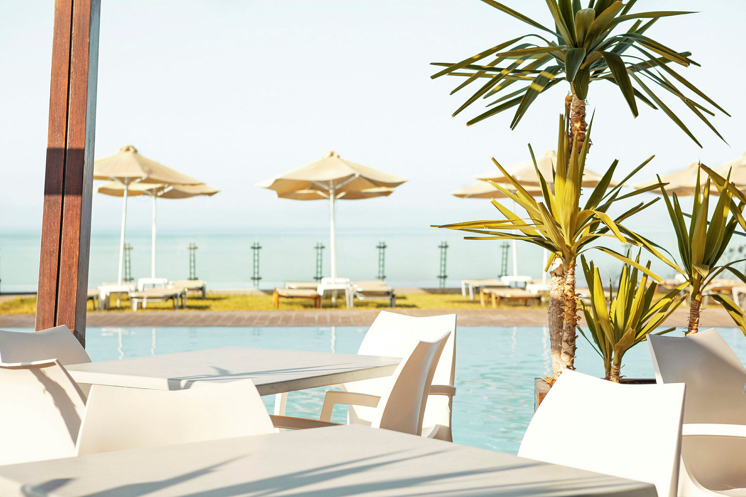 Utemöbler vid en pool med utsikt över havet och solstolar med parasoller i bakgrunden. (AI-genererad text)
