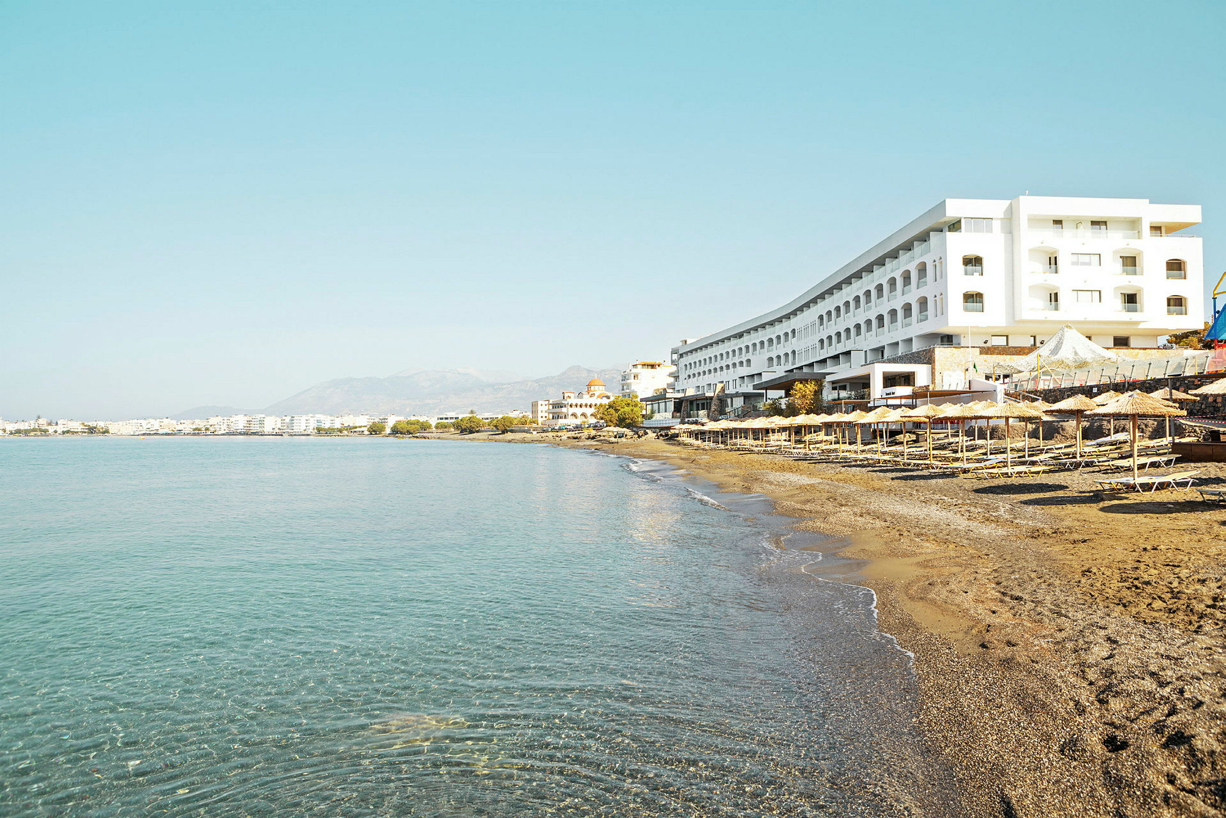 En strand med solstolar och parasoller vid foten av ett stort hotell. (AI-genererad text)