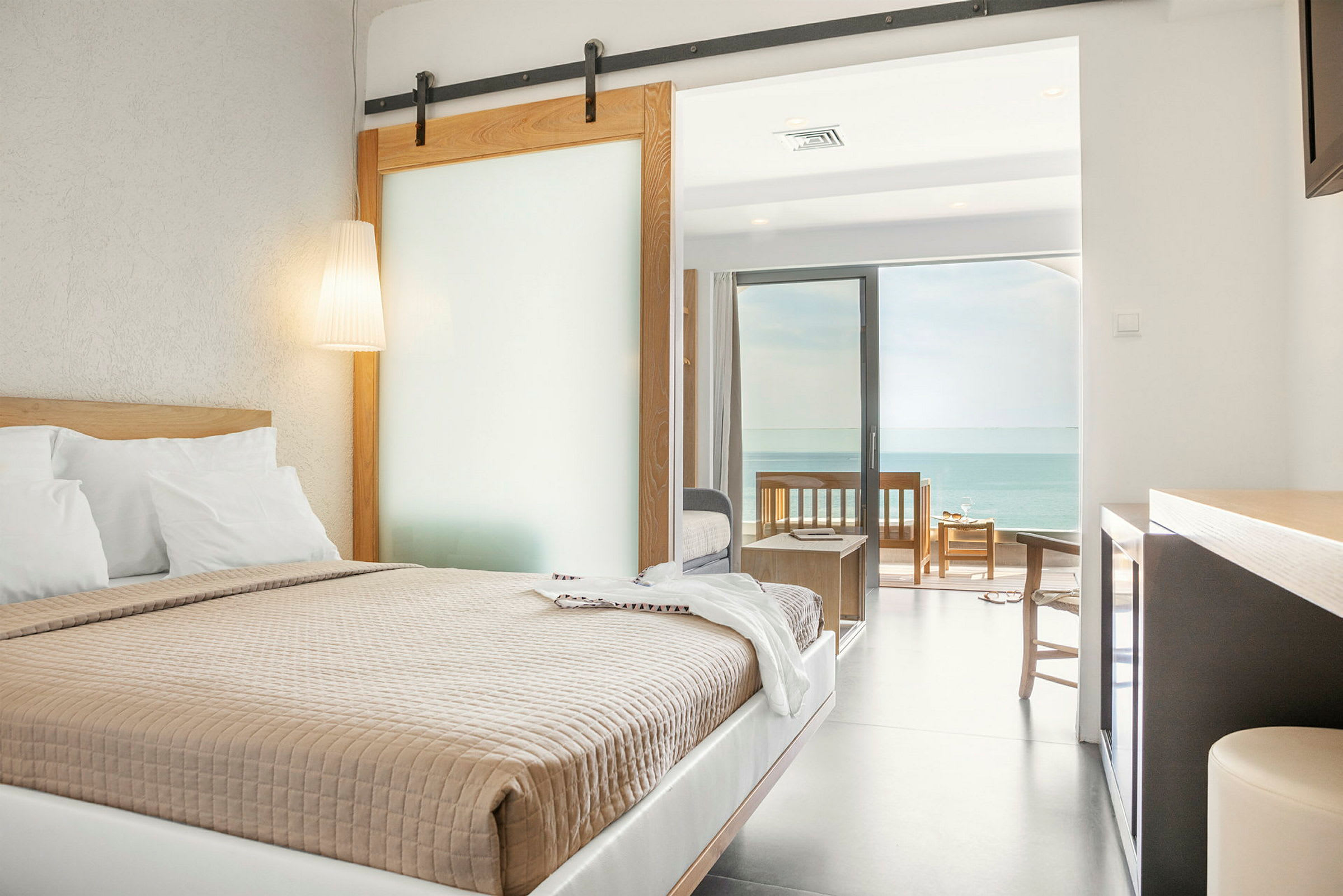 Ett hotellrum med en dubbelsäng, skjutdörr, och en terrass med utsikt över havet. (AI-genererad text)