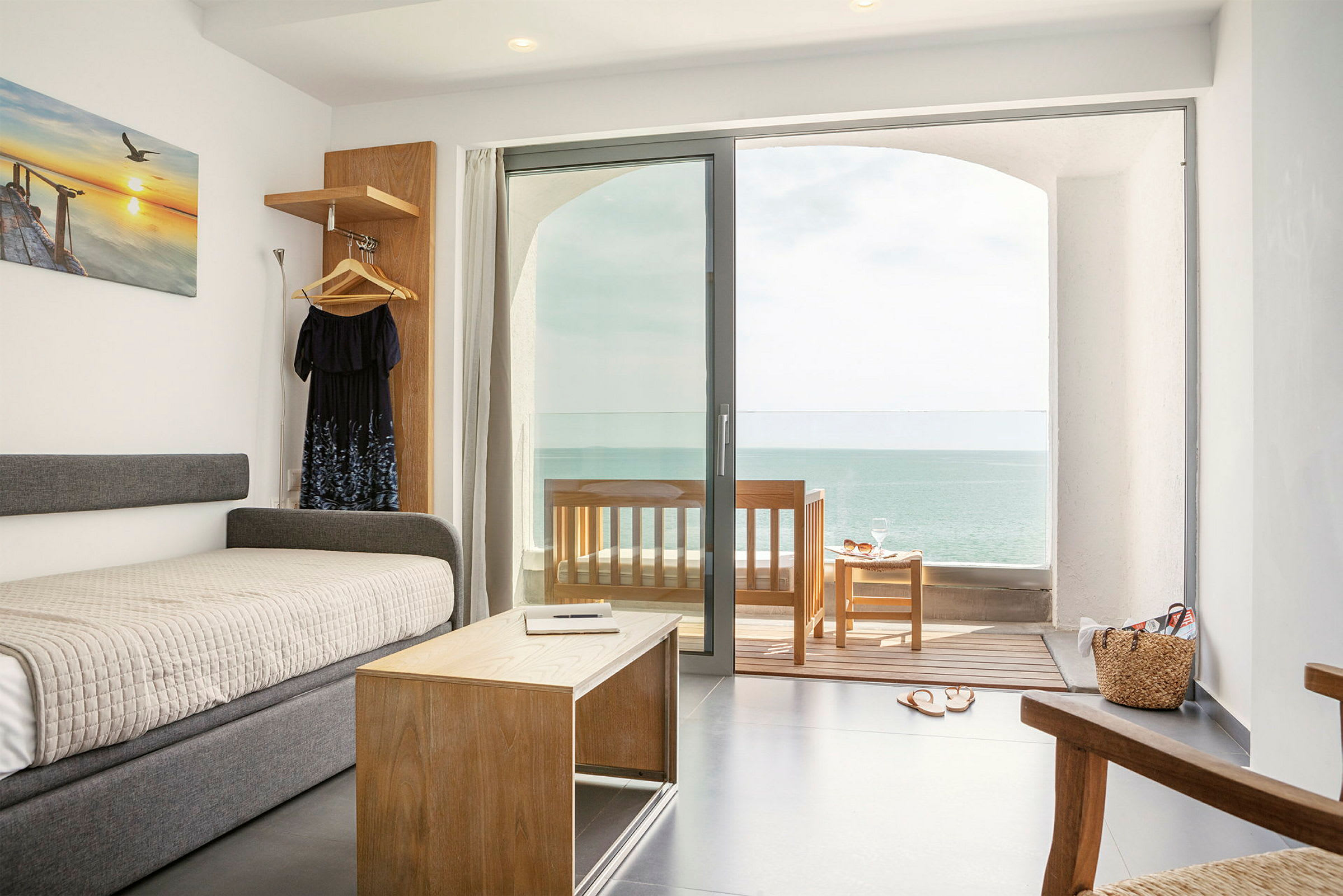 Ett hotellrum med havsutsikt. En säng och ett soffbord framför en glasdörr som leder ut till en veranda. (AI-genererad text)