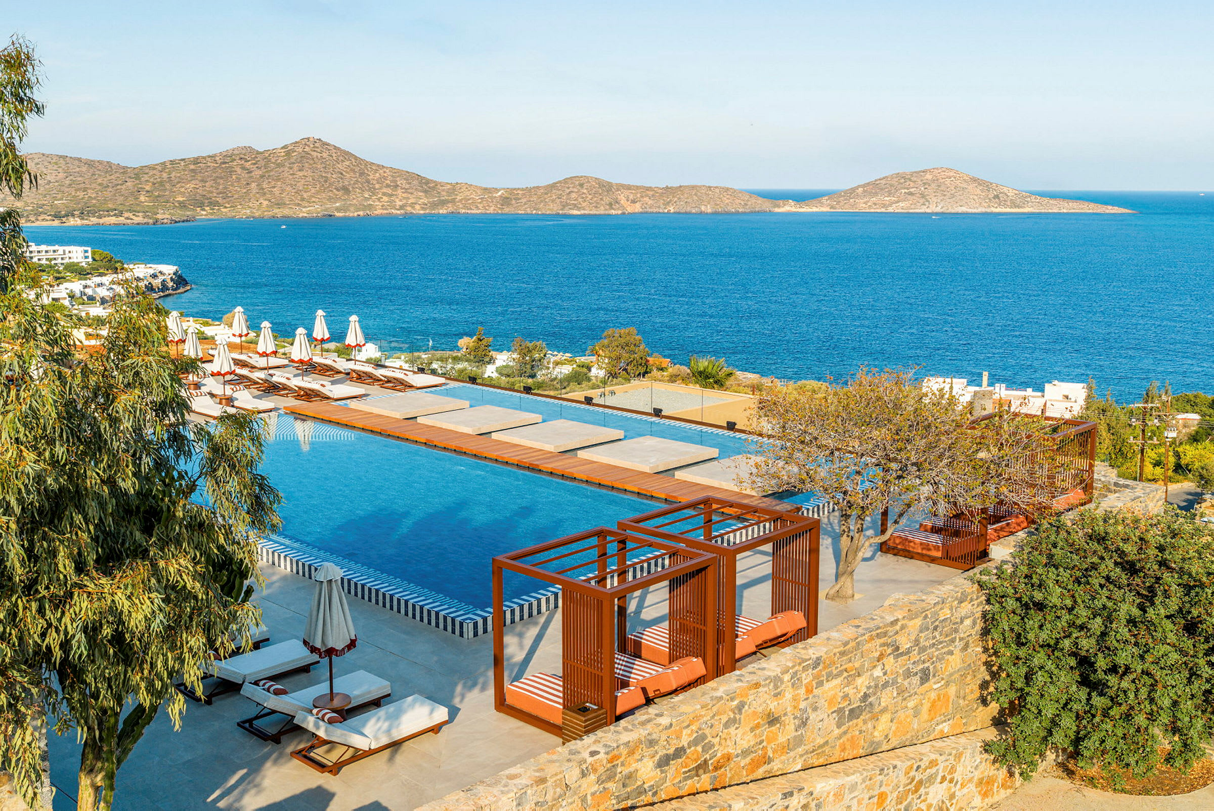 En lyxig pool med solsängar och cabanas vid havet på en solig dag. (AI-genererad text)