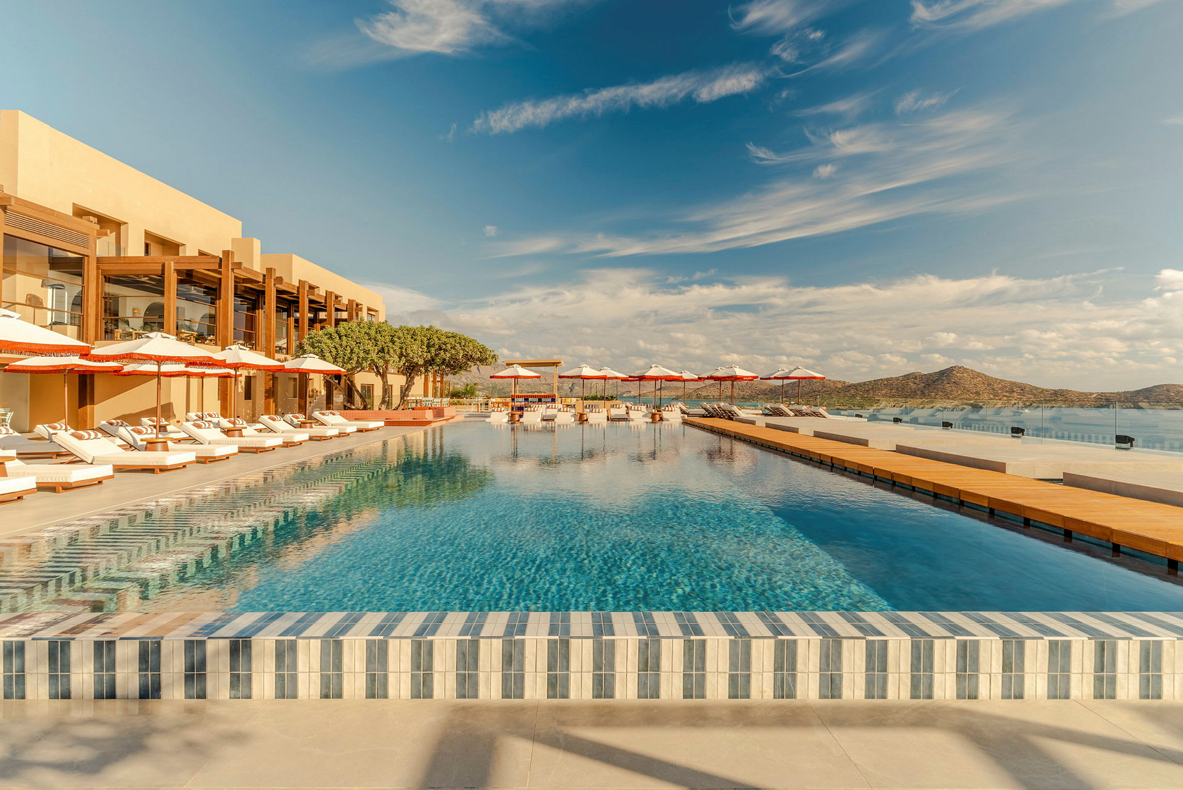 Bild av en elegant pool med solstolar och parasoller vid sidan och berg i bakgrunden. (AI-genererad text)
