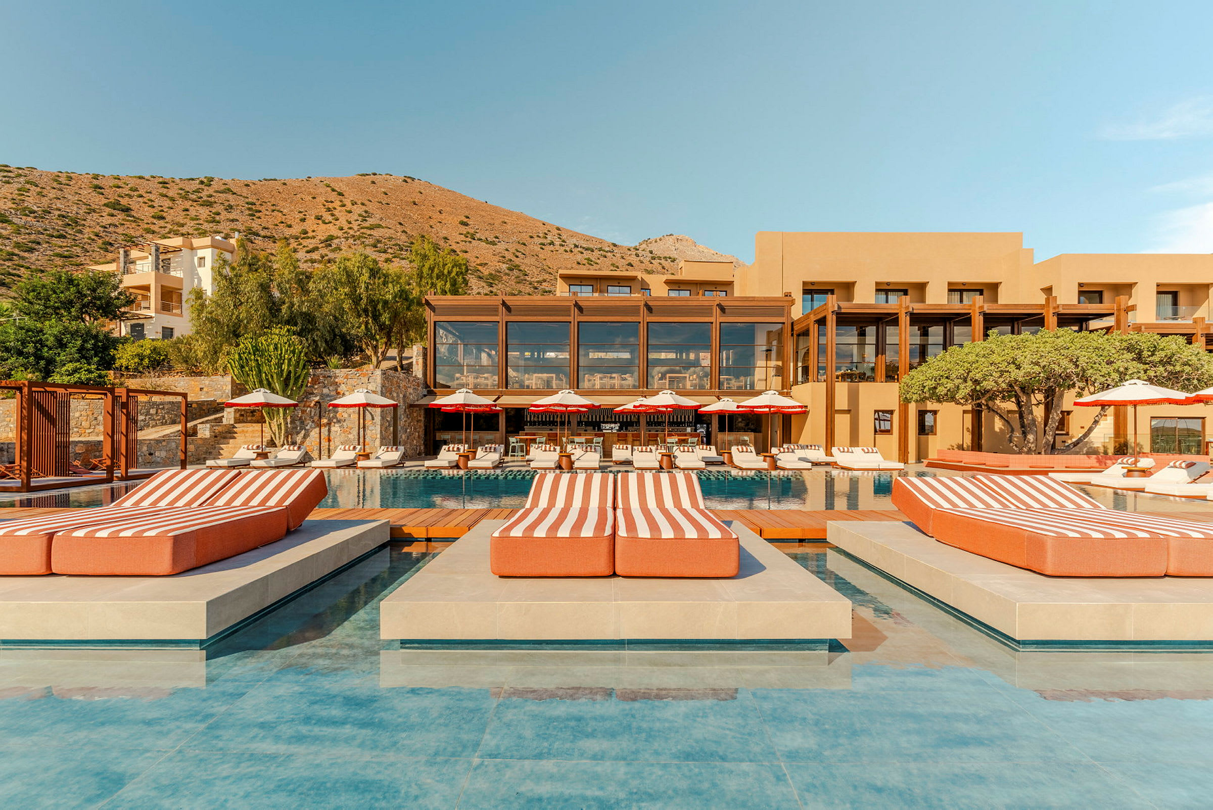 Ett lyxigt hotellkomplex med pool, solstolar och en bergig bakgrund. (AI-genererad text)