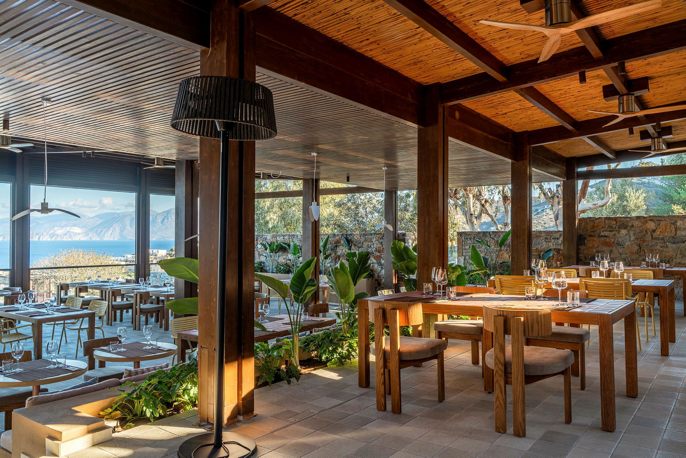 En utomhusrestaurang med träinredning och utsikt över havet och bergen. (AI-genererad text)