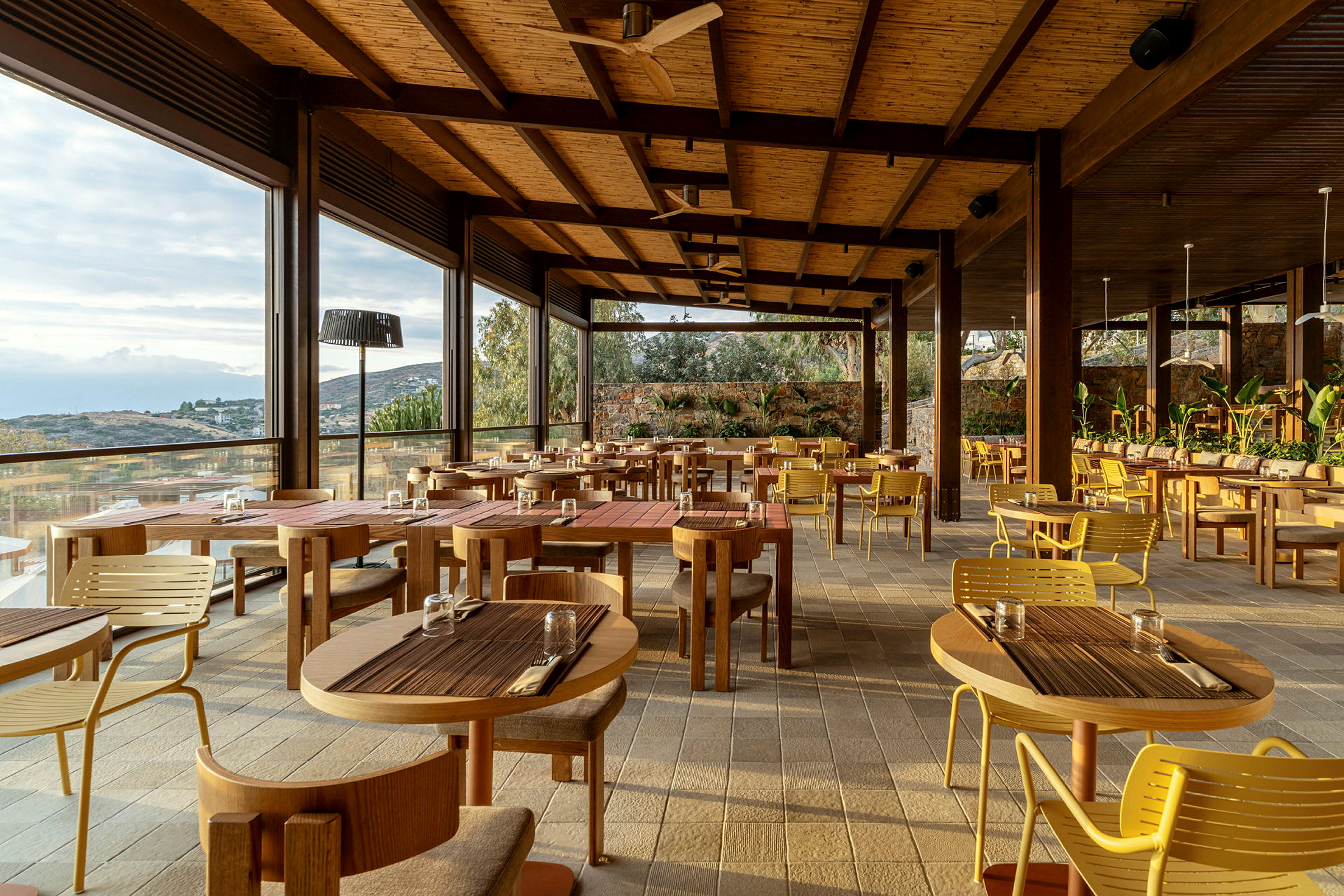 En restaurang med träbord och stolar, omsluten av stora fönster med utsikt över landskapet. (AI-genererad text)