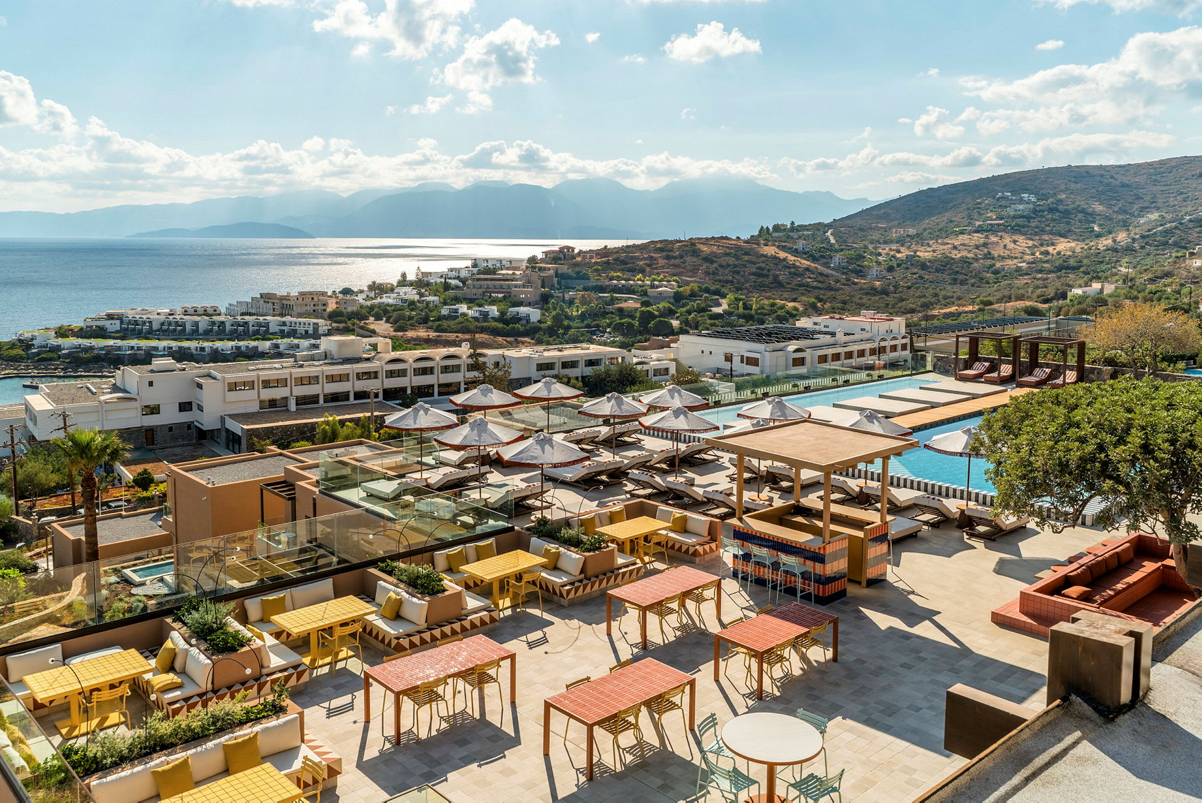 Bild av en hotellresort med en solig terrass, poolområde och utsikt över havet och kullar. (AI-genererad text)