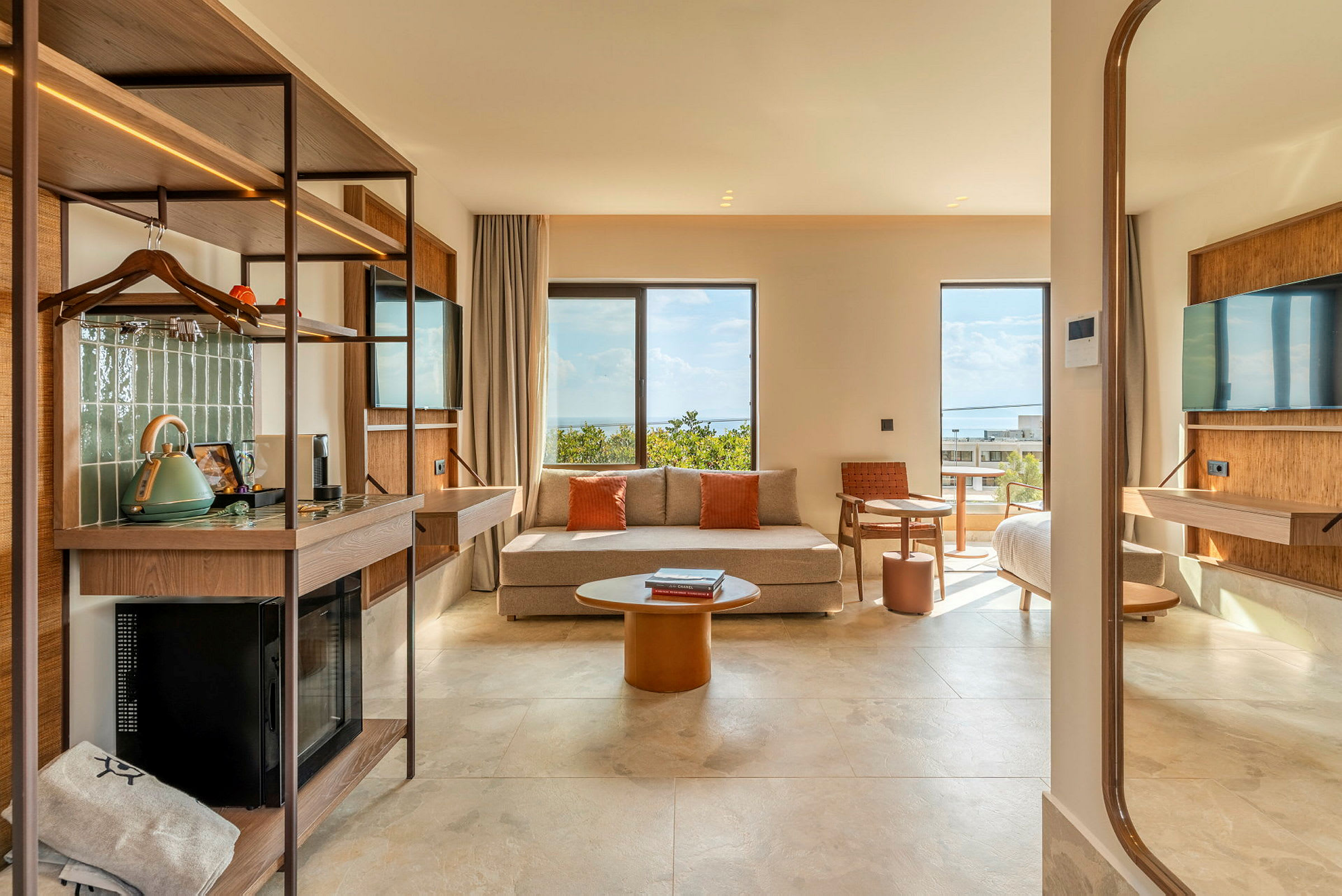Ett modernt hotellrum med soffa, tv, bord och säng. Utsikt över havet genom stora fönster. (AI-genererad text)