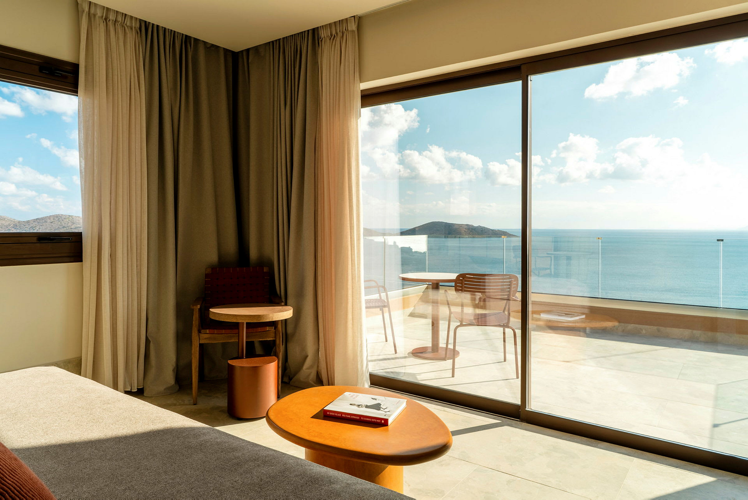 Modernt hotellrum med stora glasdörrar som vetter mot en balkong med havsutsikt. (AI-genererad text)