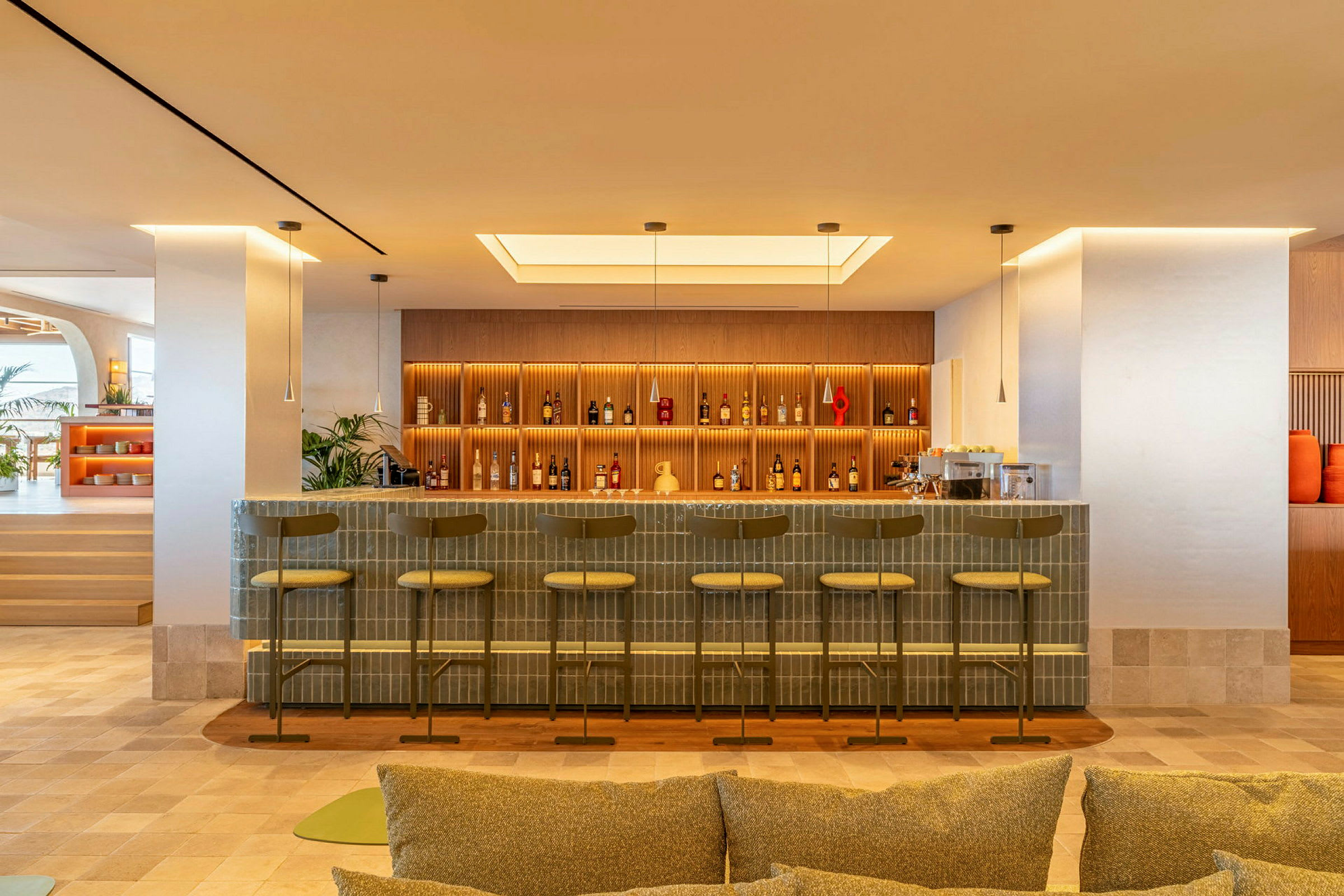 En modern bar med stolar vid disken och flaskor på hyllor i bakgrunden. Varm belysning och elegant design. (AI-genererad text)