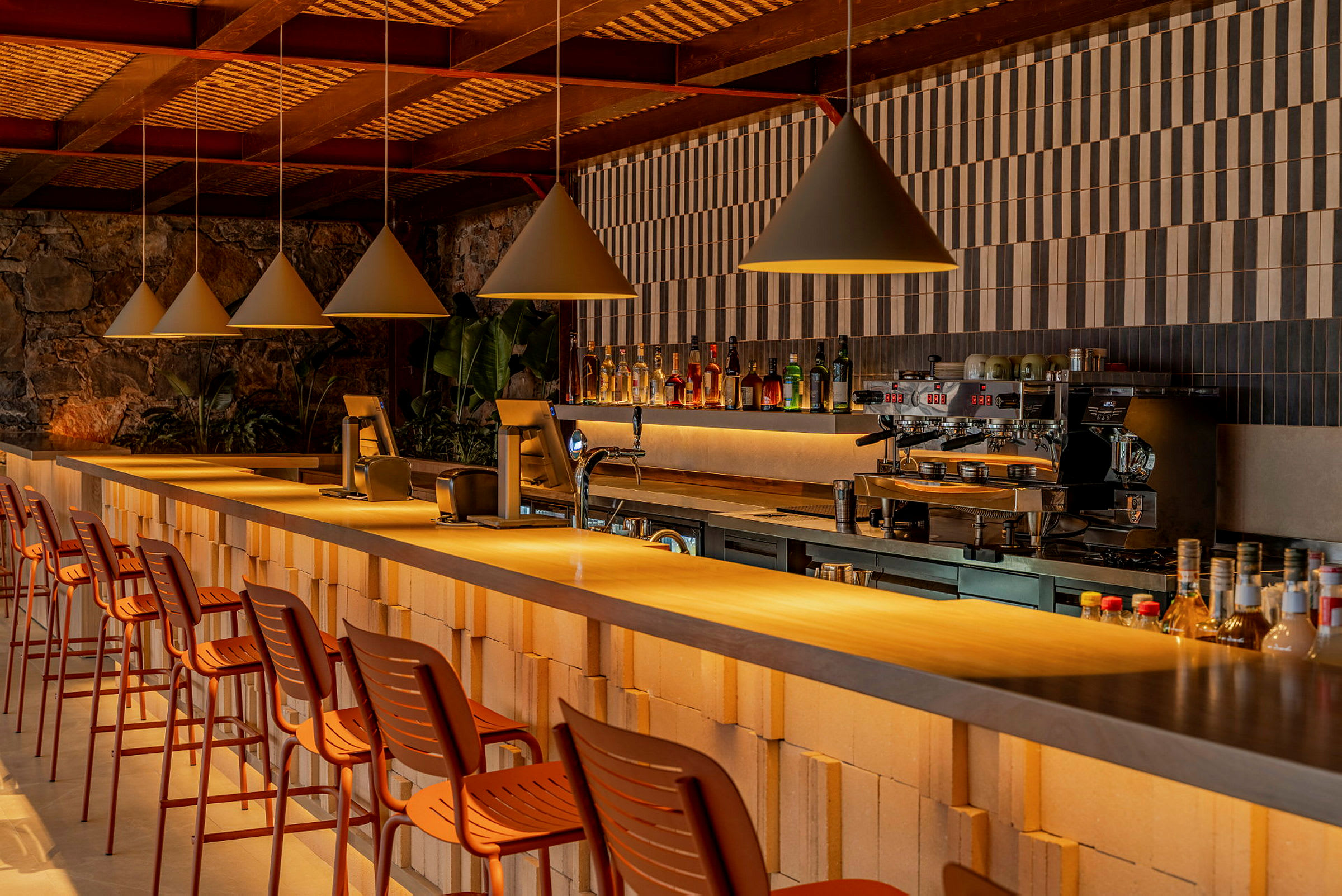 Interiör av en bar med höga stolar och belysning hängande ovanför en lång bardisk. (AI-genererad text)