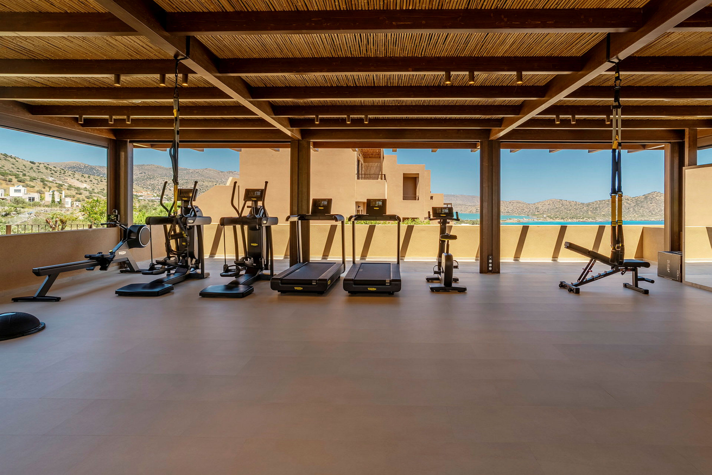 Ett gym med träningsutrustning, såsom löpband, träningscyklar och styrketräningsredskap, under ett tak med utsikt över bergen. (AI-genererad text)