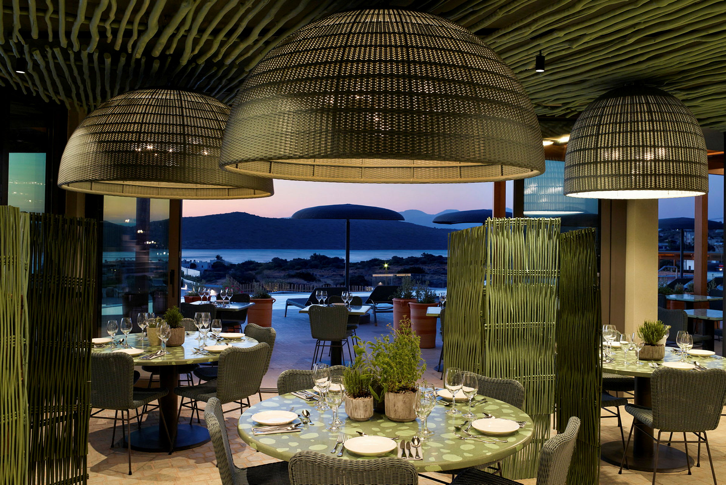 Restaurang med dukade bord och stora lampkupor, utsikt mot havet i solnedgången. (AI-genererad text)
