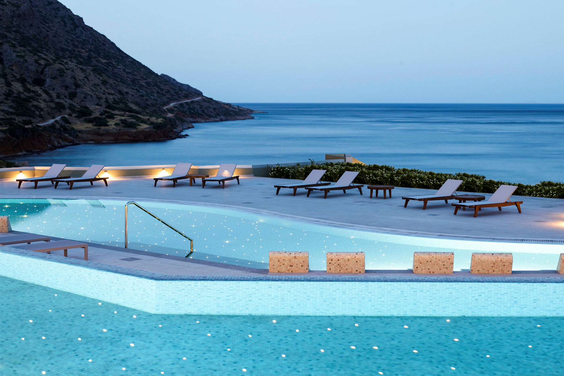 Utsikt över en pool med solstolar och hav i bakgrunden. (AI-genererad text)