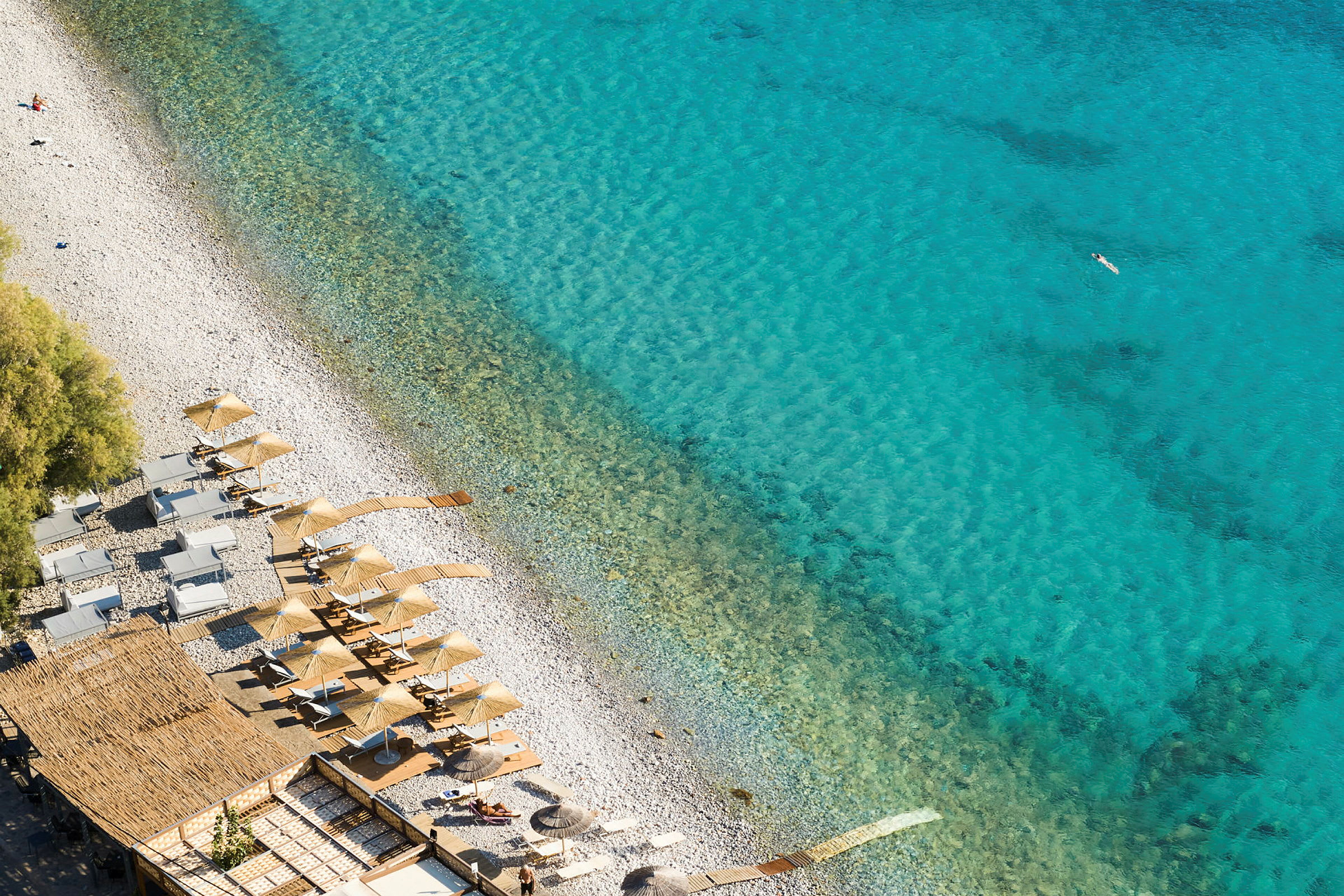 Vy över en strand med parasoller och solstolar vid klart blått vatten. (AI-genererad text)