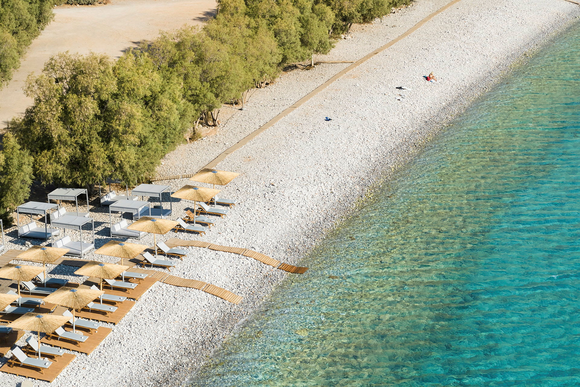 En stenig strand med solstolar, parasoller och träspångar nära klart vatten. (AI-genererad text)