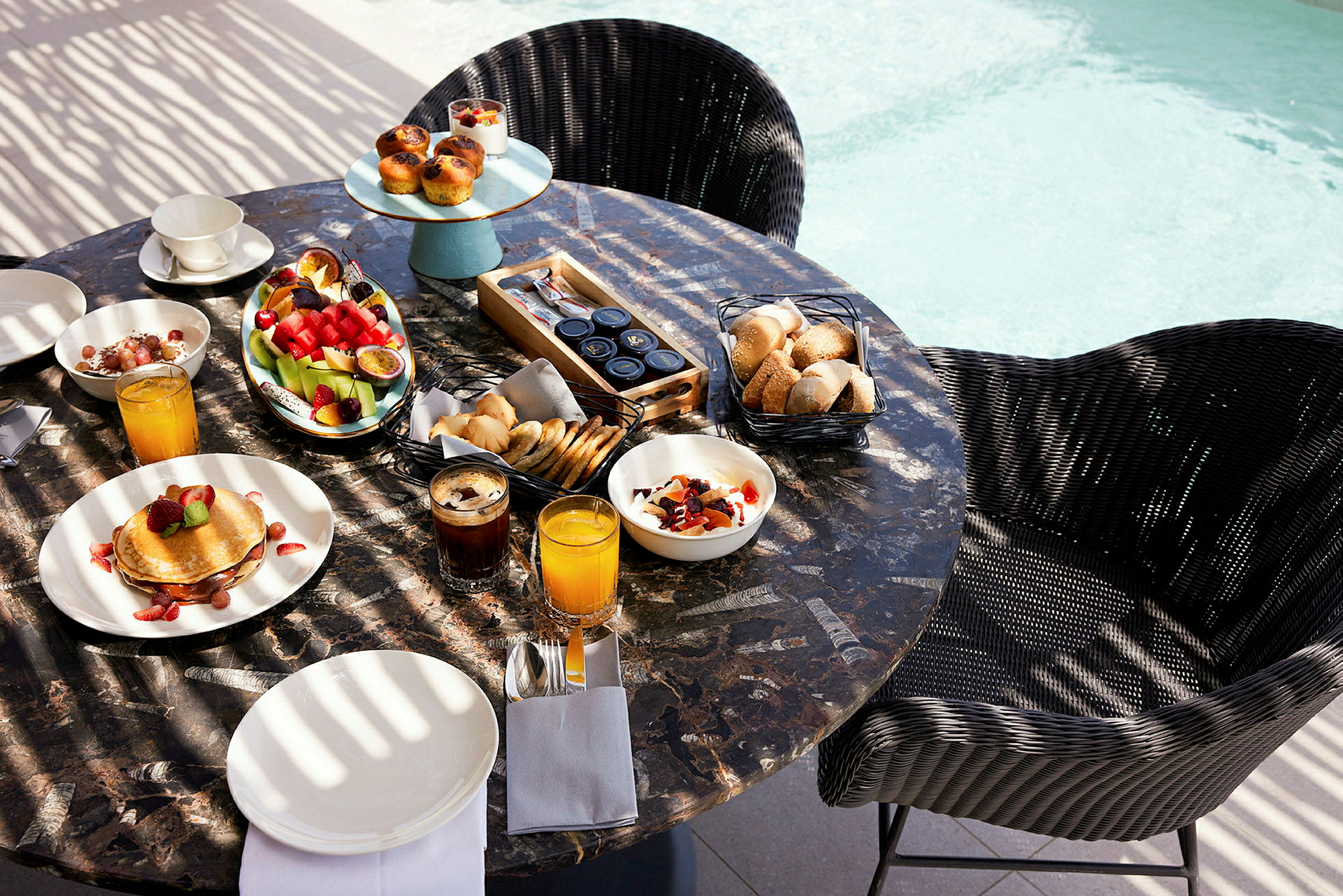 Frukostbord med olika maträtter och drycker vid poolkanten. (AI-genererad text)