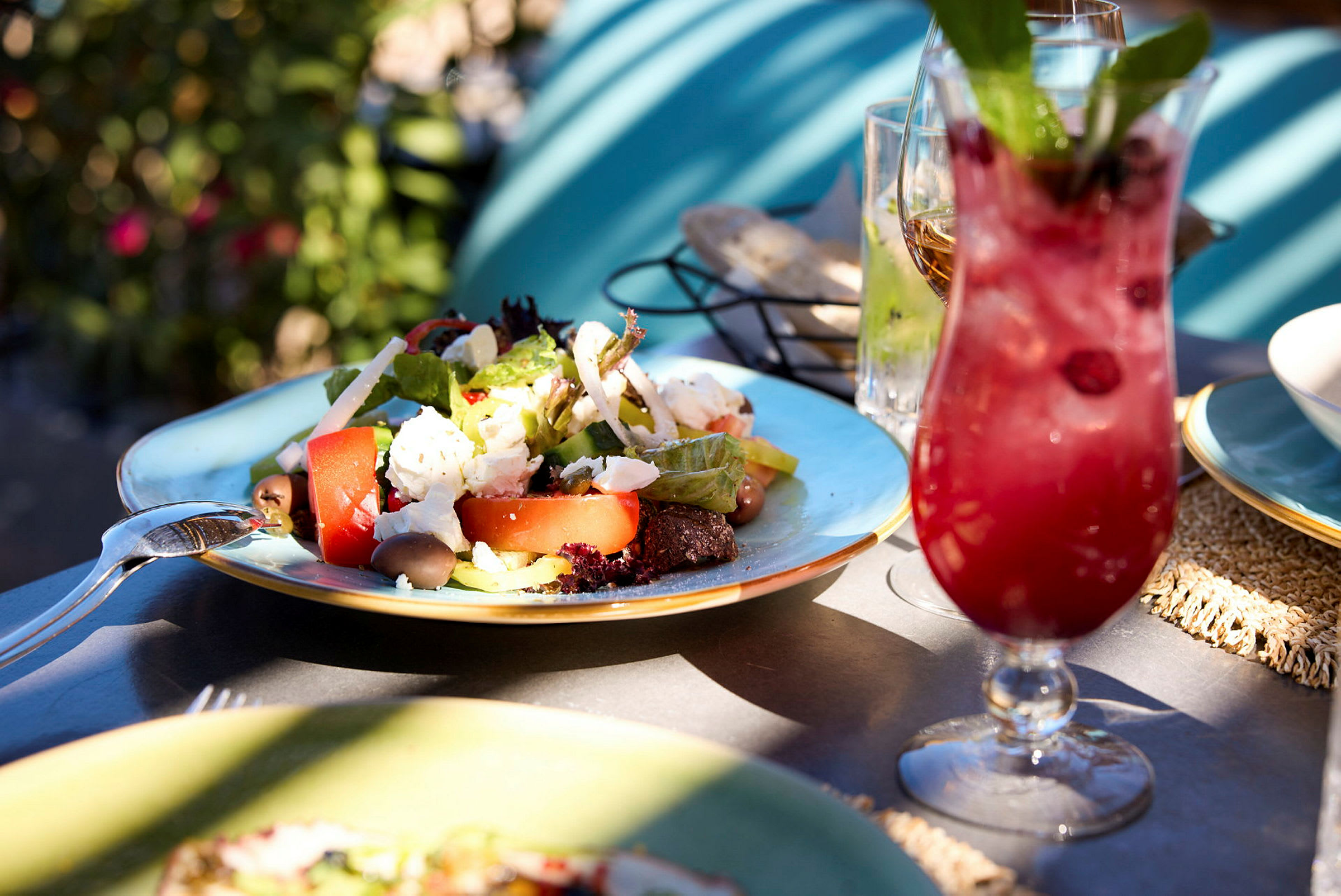 En tallrik med sallad och en röd drink på ett bord utomhus. (AI-genererad text)
