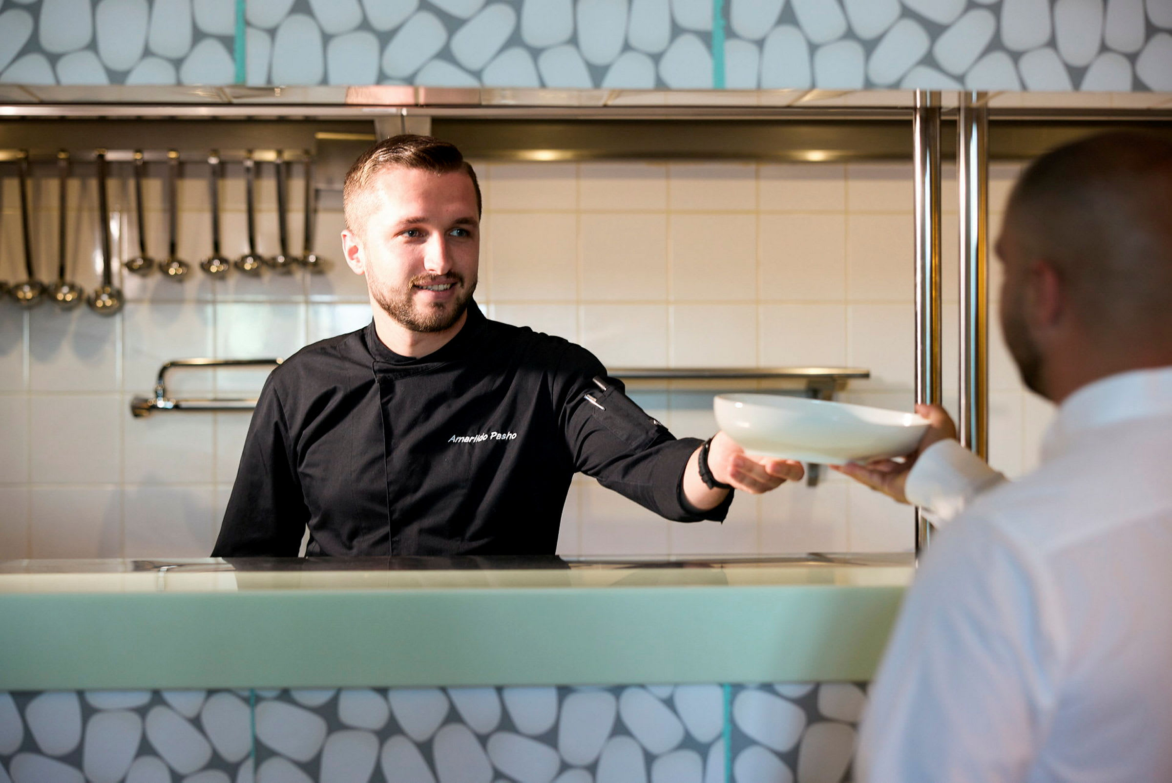 En person i kockkläder överräcker en skål till en annan person. (AI-genererad text)