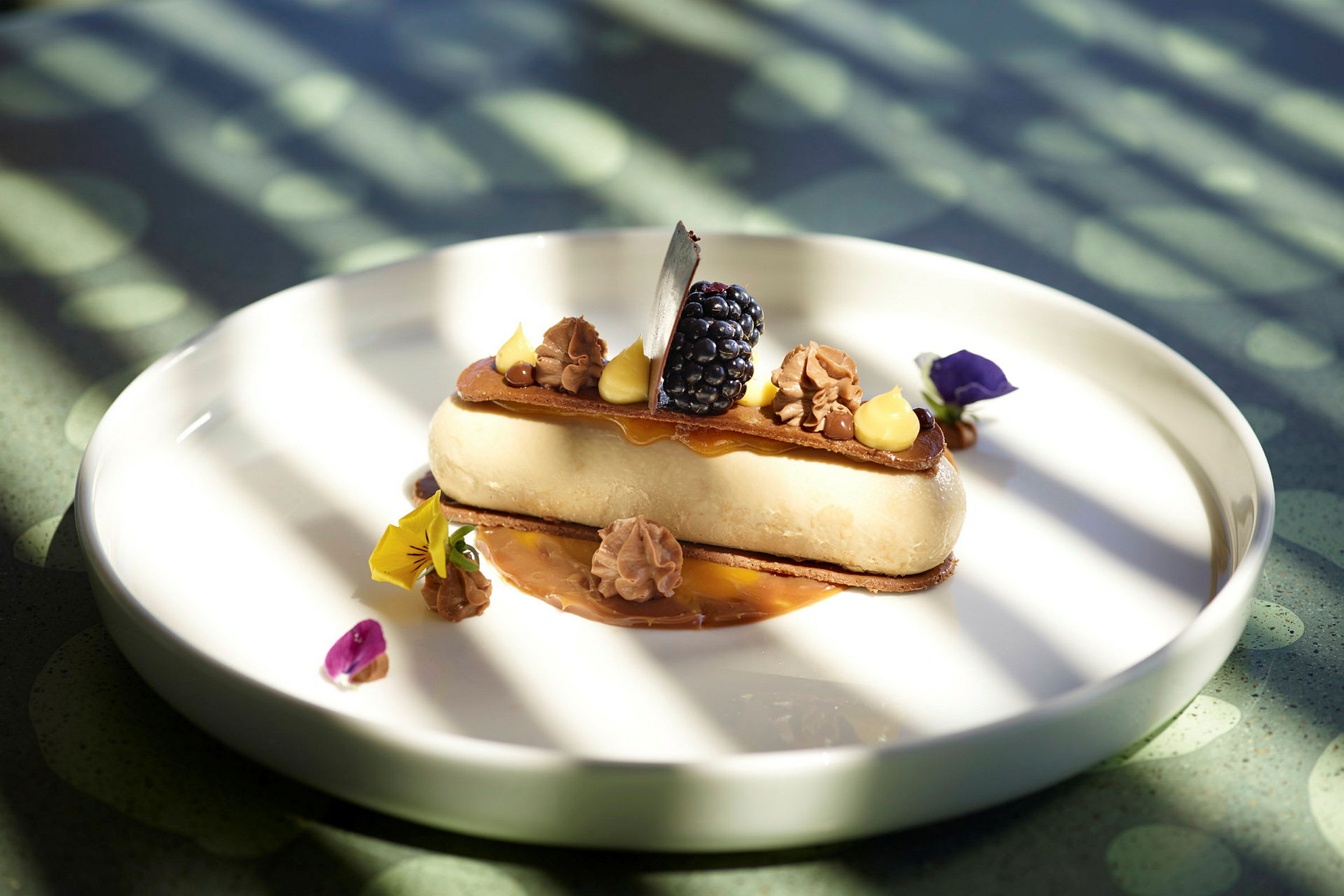 Dessert serverad på en vit tallrik, dekorerad med grädde, bär och ätbara blommor. (AI-genererad text)
