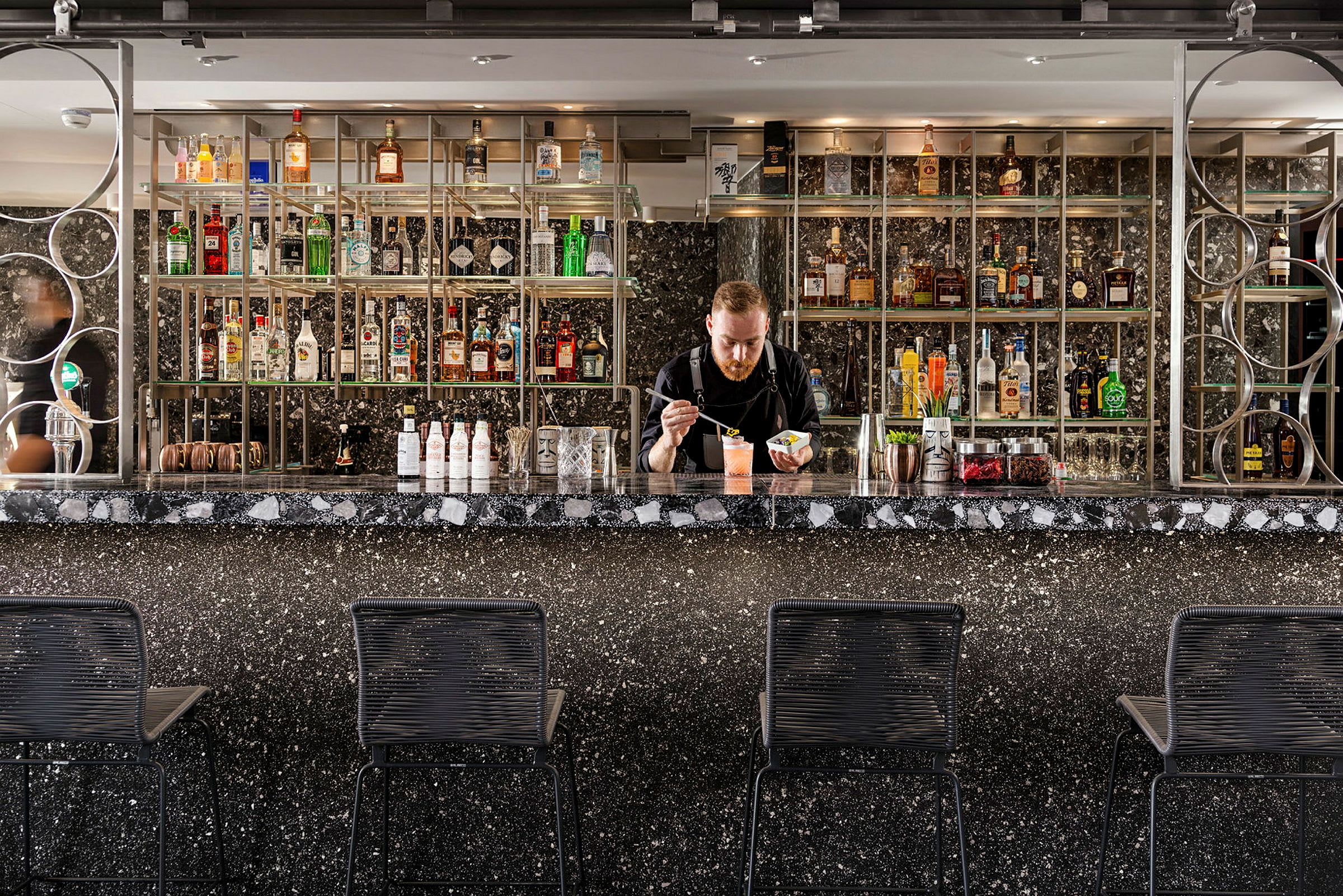 En elegant bar med svart marmorbardisk och hyllor fyllda med spritflaskor. (AI-genererad text)