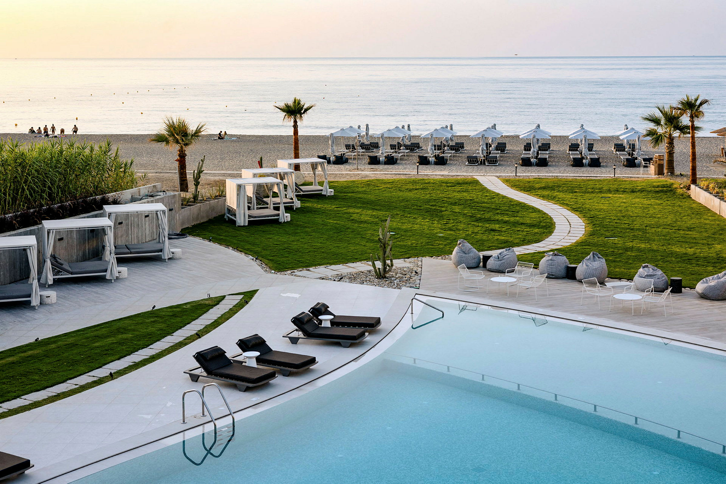 En semesteranläggning vid stranden med solstolar, gräsmattor, cabanas och en pool. (AI-genererad text)