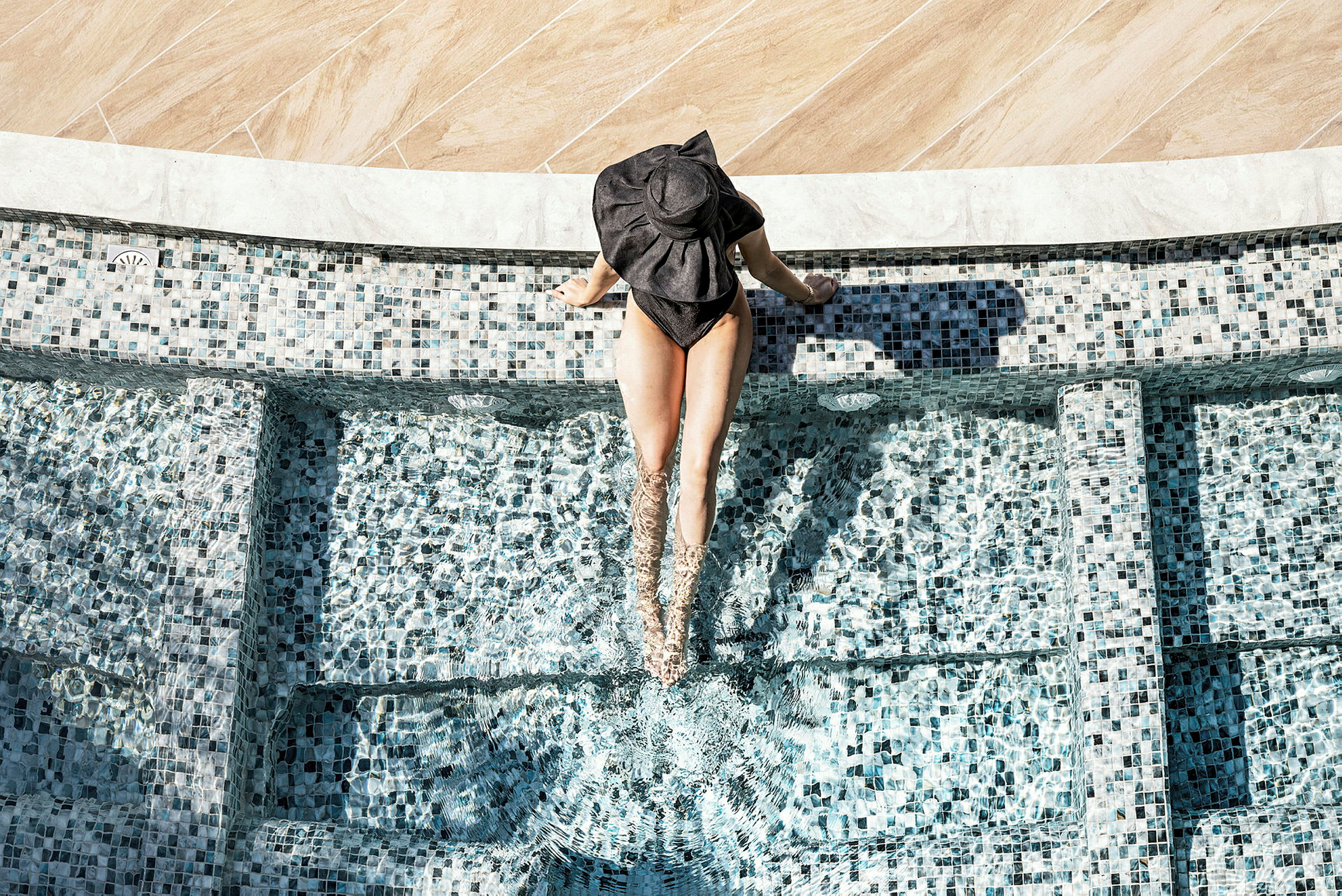 En person sitter vid kanten av en mosaikprydd pool med benen i vattnet. (AI-genererad text)