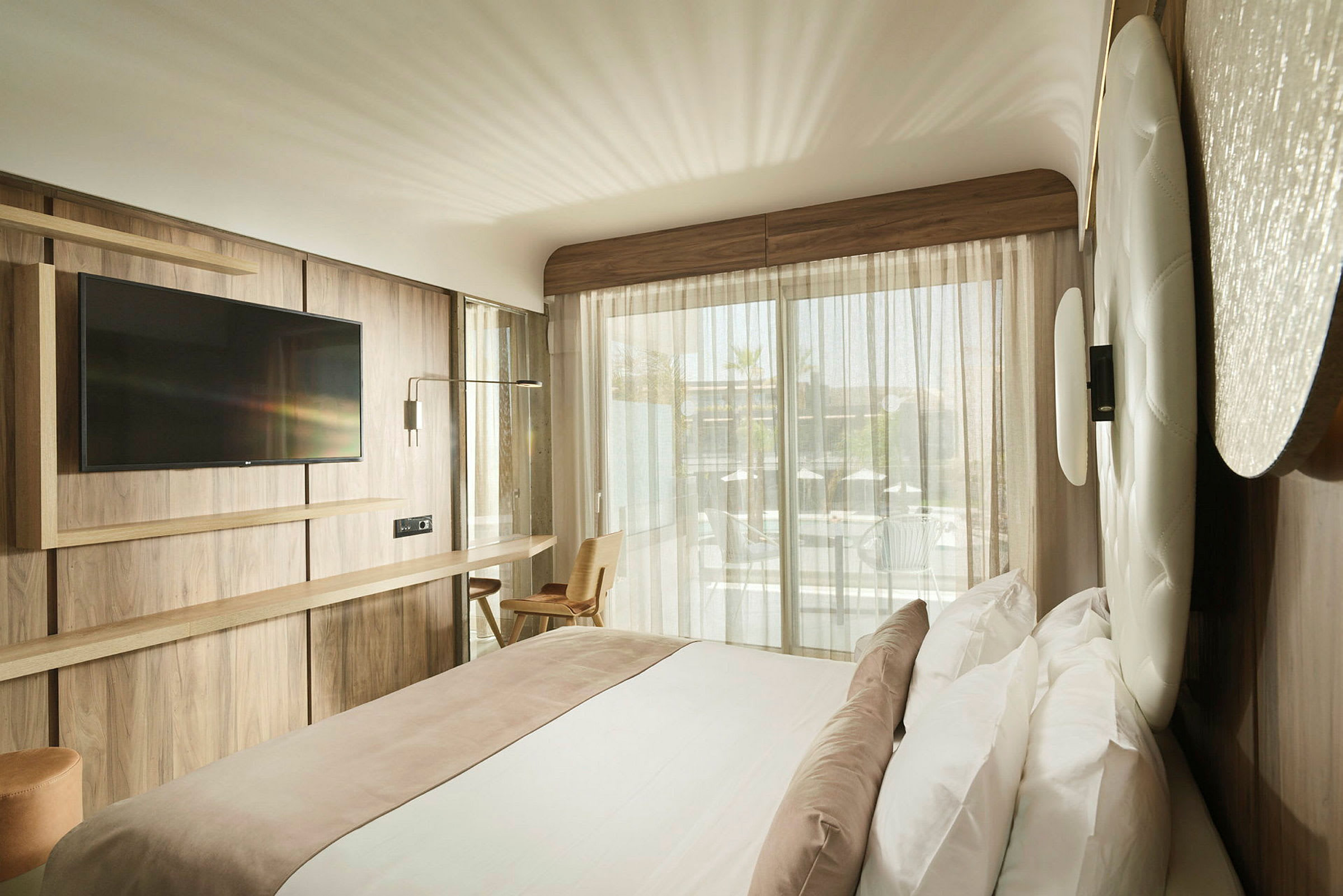 Modernt hotellrum med dubbelsäng, väggmonterad TV och stort fönster mot en balkong. (AI-genererad text)