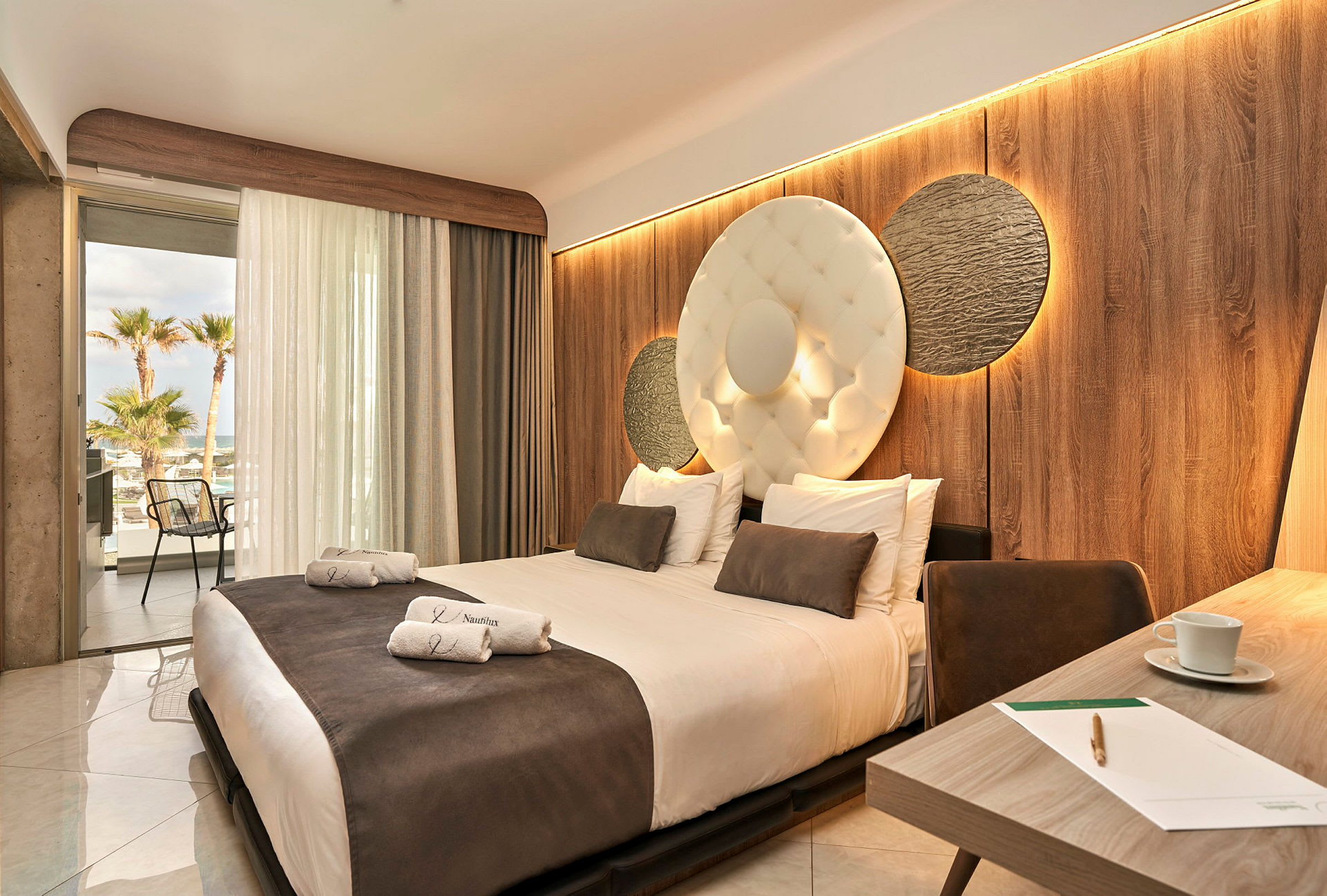 Hotellrum med en stor säng, dekorerad vägg och öppen balkong med utsikt. (AI-genererad text)