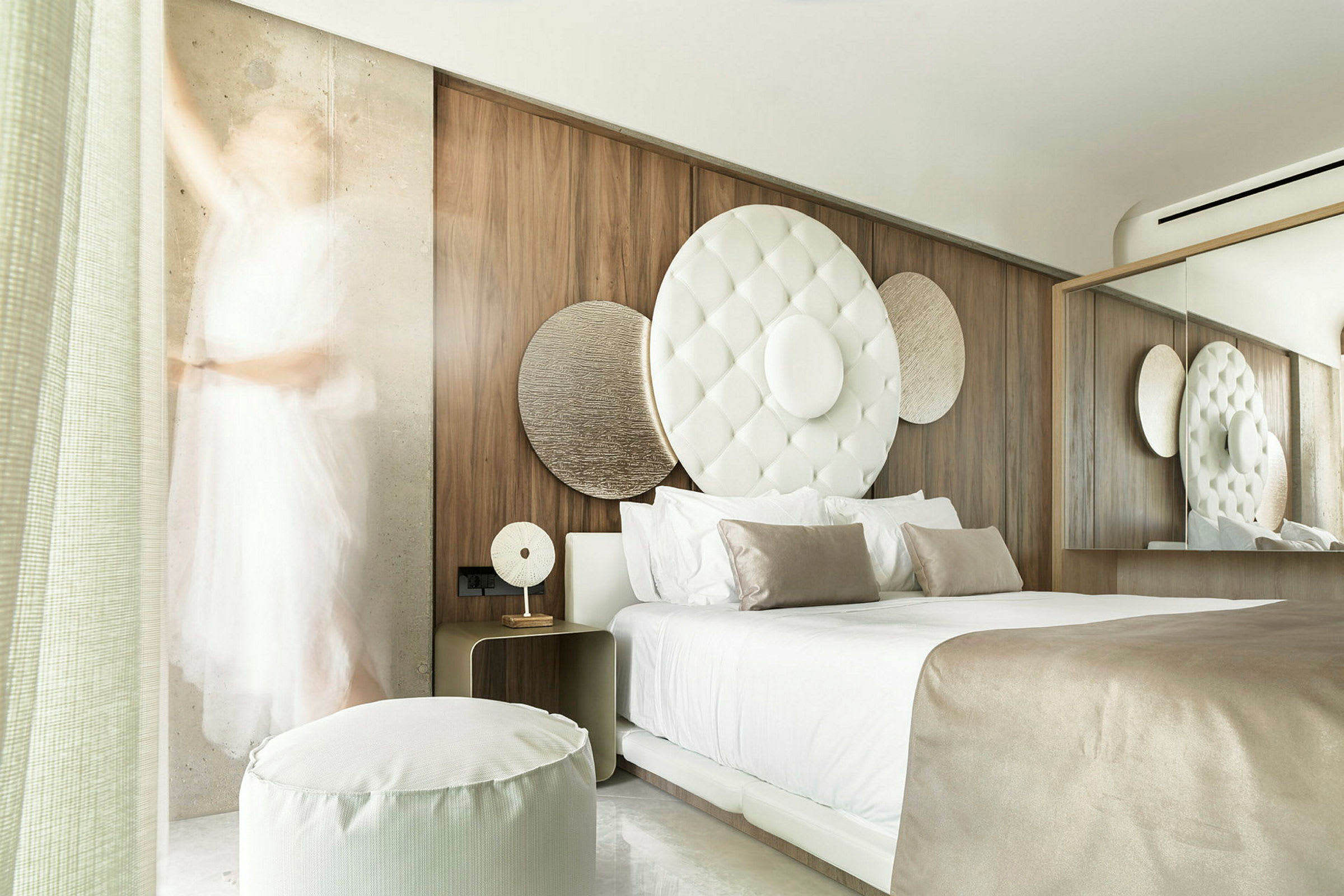 Ett modernt hotellrum med en stor säng, dekorativa cirkulära element på väggen och mjuka beige och vita färger. (AI-genererad text)