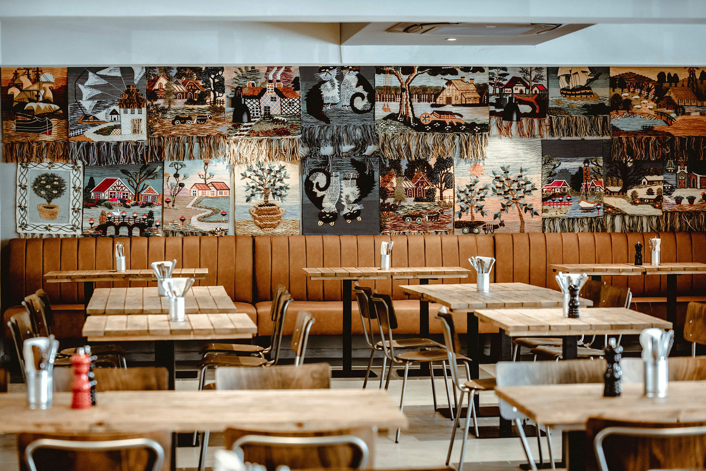 Restaurang med träbord och stolar samt väggdekorationer med broderade motiv. (AI-genererad text)