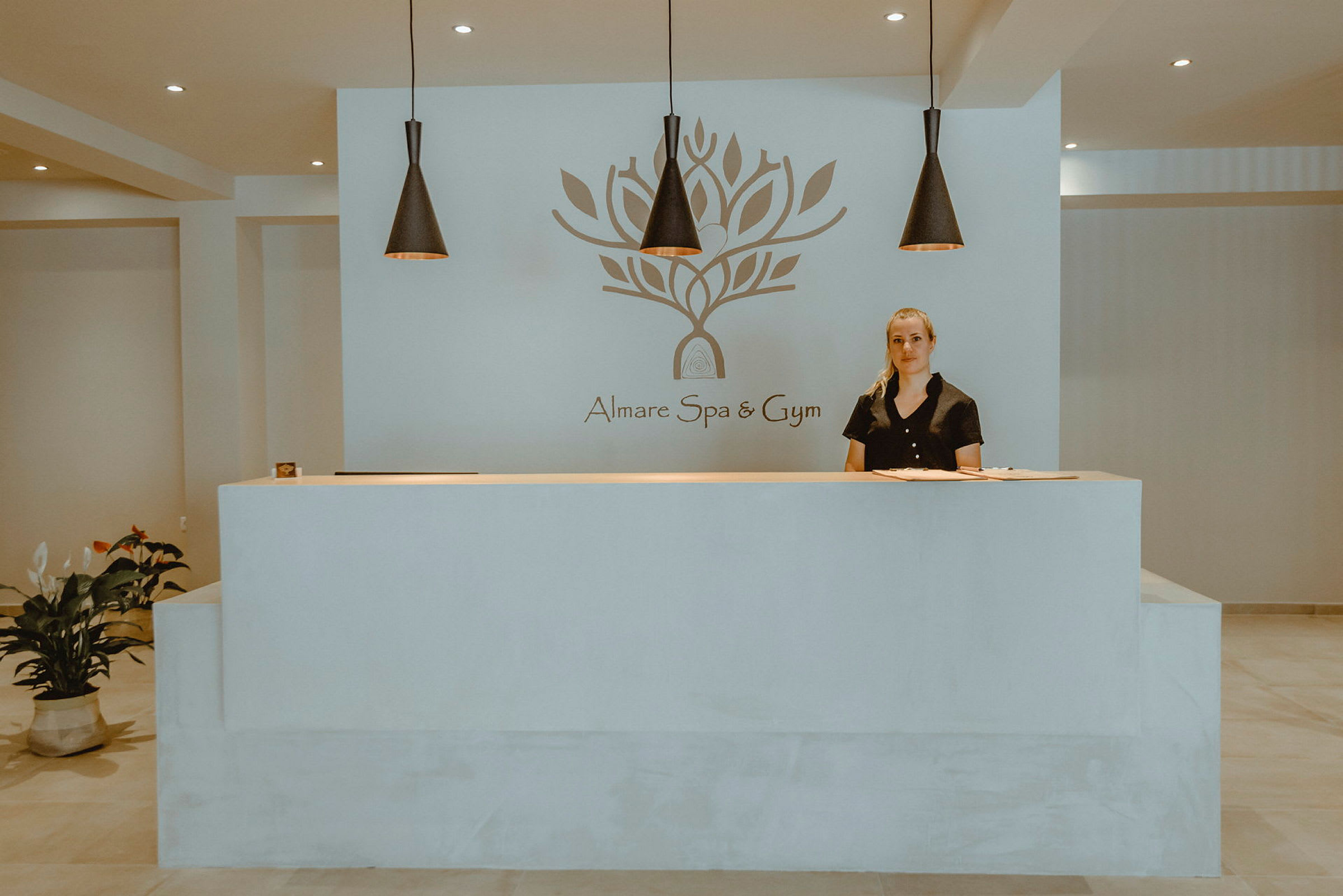 Receptionen vid Almare Spa och Gym med en logotyp på väggen och dekorativ belysning ovanför. (AI-genererad text)