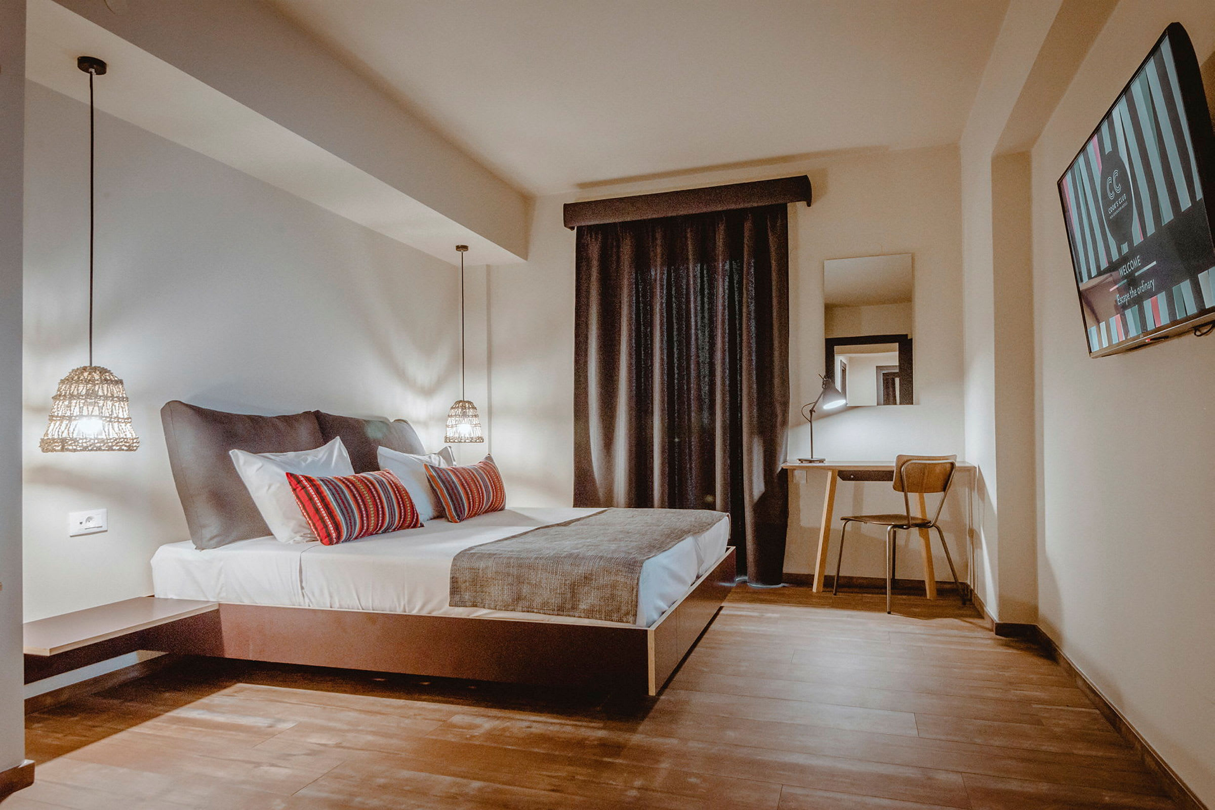 Ett hotellrum med en dubbelsäng, skrivbord och stol samt en tv på väggen. (AI-genererad text)