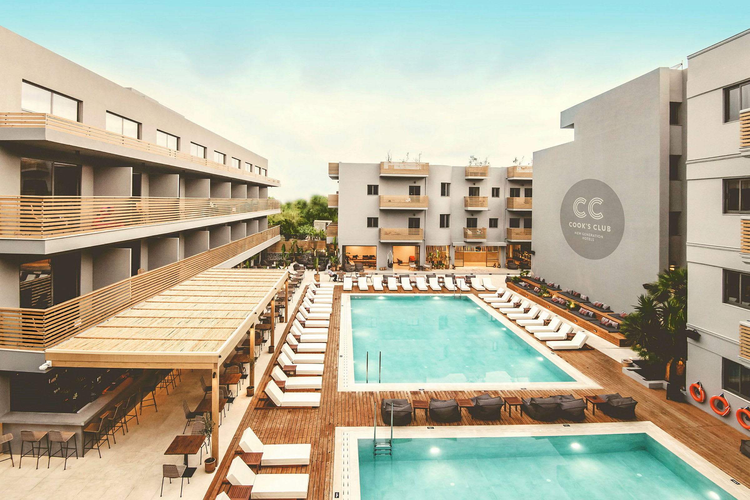 Utsikt över hotell med poolområde, solstolar och byggnader. (AI-genererad text)