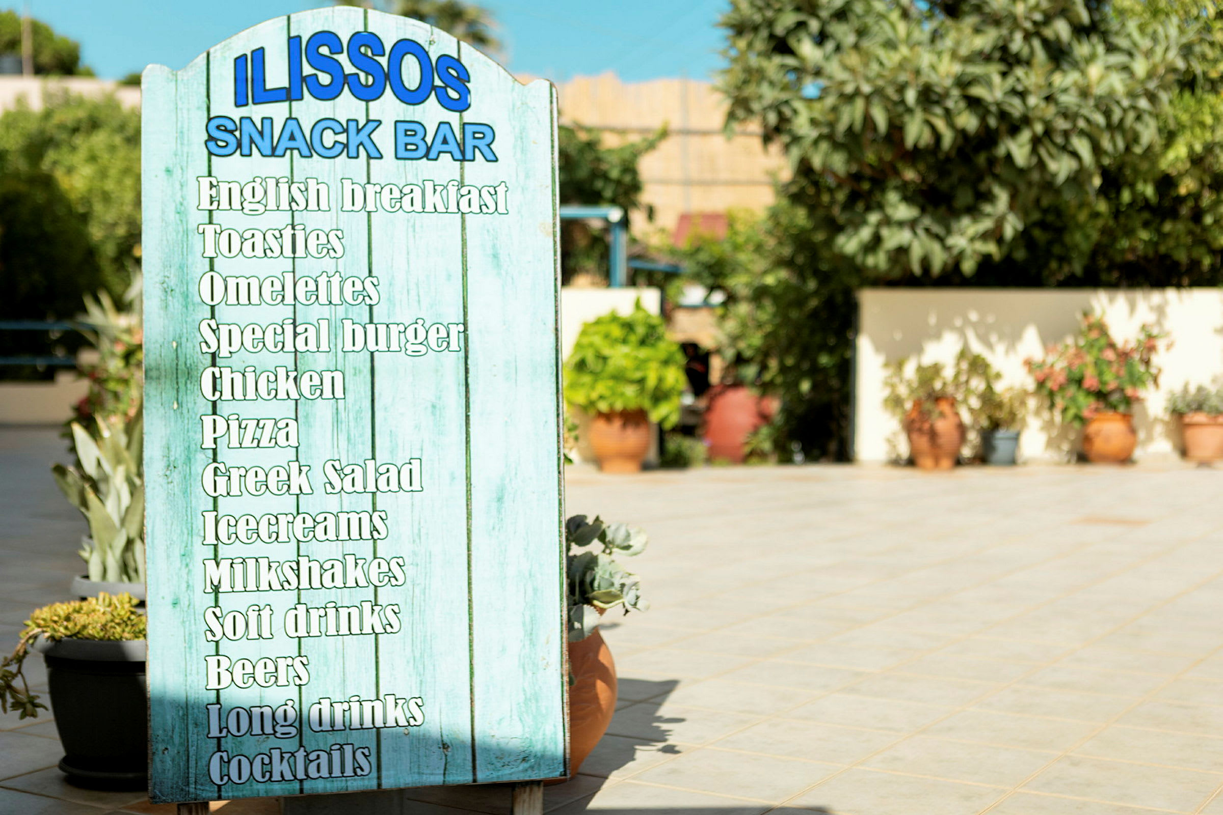Skylt som visar menyn på Ilissos Snack Bar med olika maträtter och drycker. (AI-genererad text)