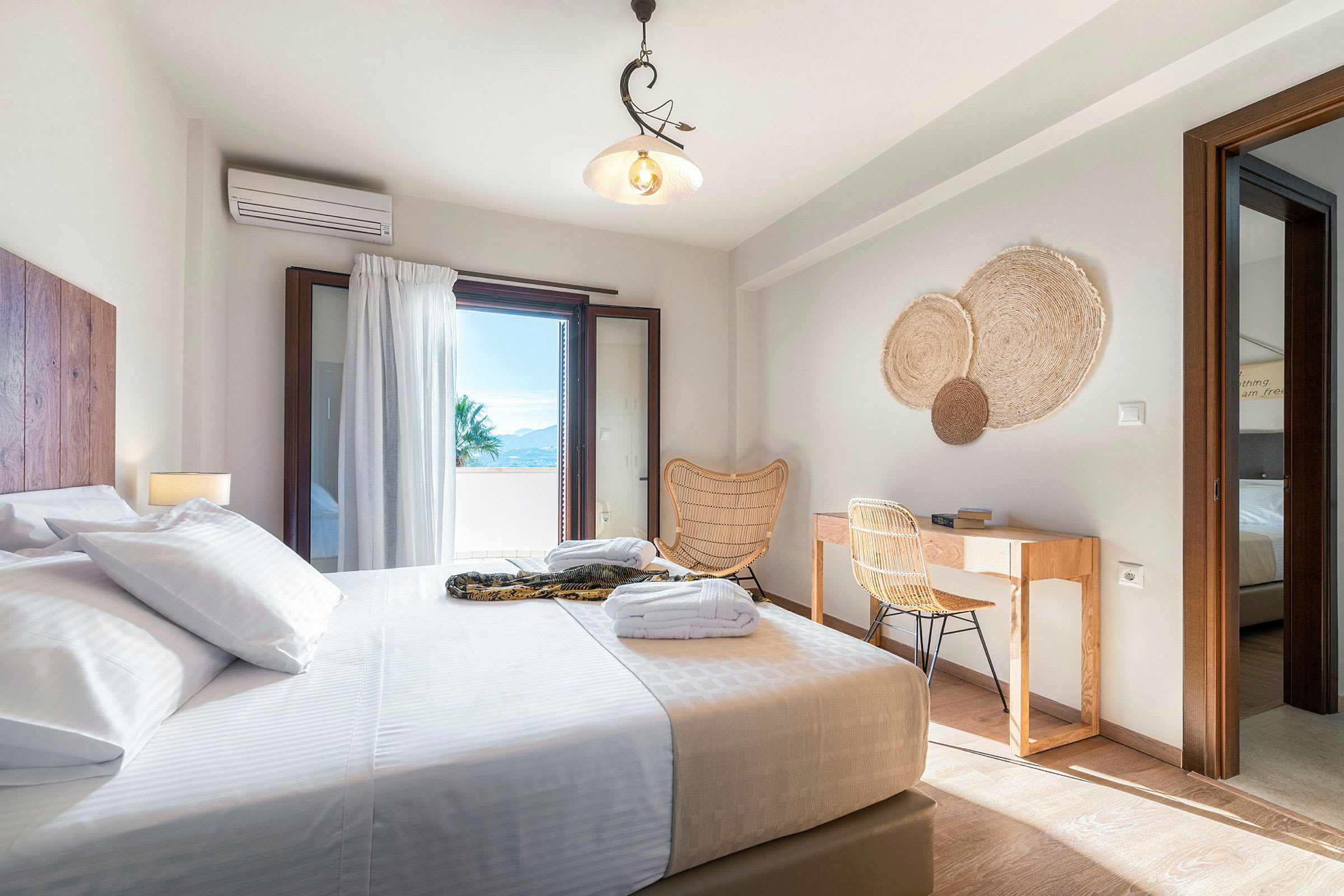 Ett ljust hotellrum med säng, skrivbord och en öppning mot en balkong. (AI-genererad text)