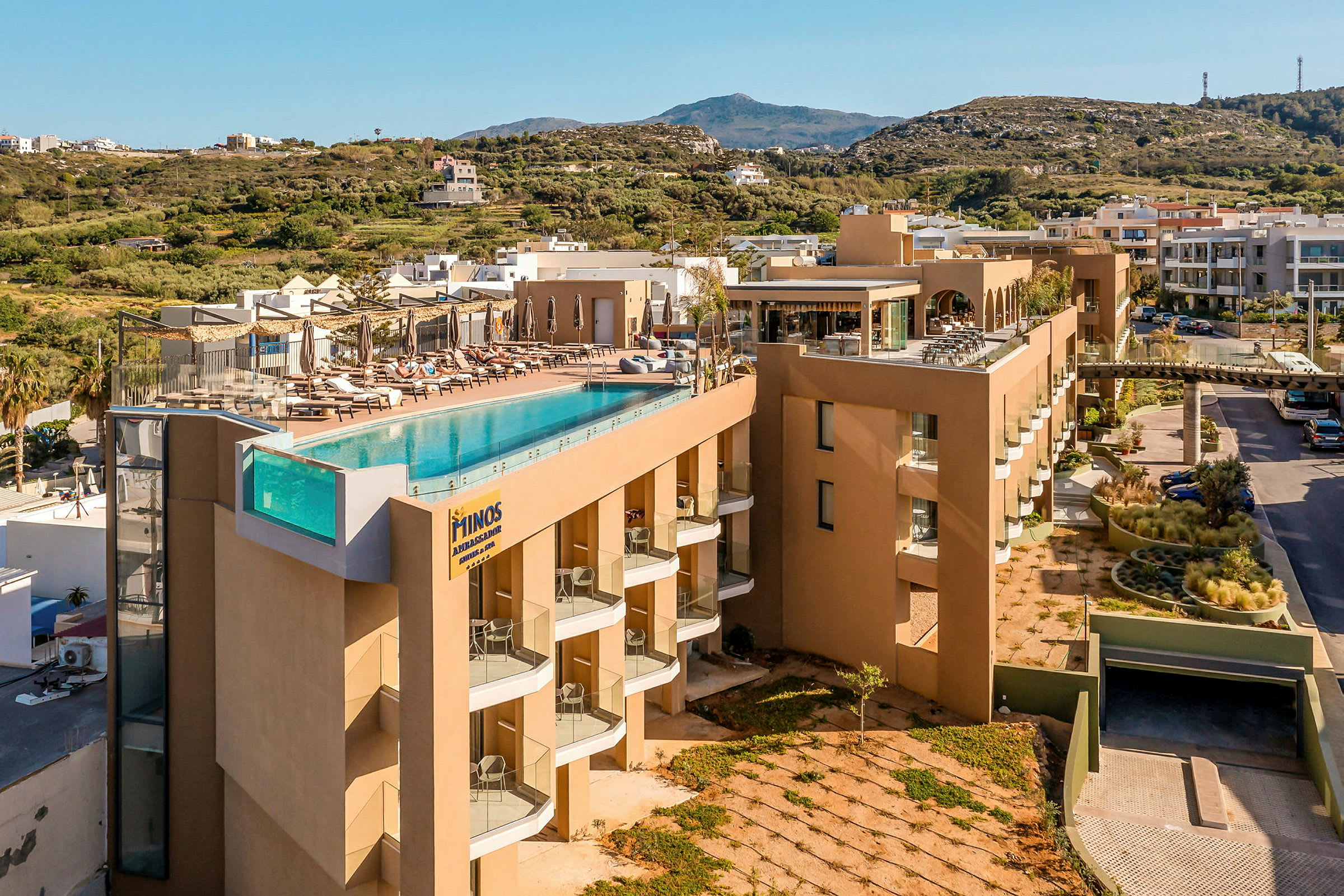Ett hotell med en infinitypool på taket, omgiven av solstolar och med utsikt över grönska och berg. (AI-genererad text)