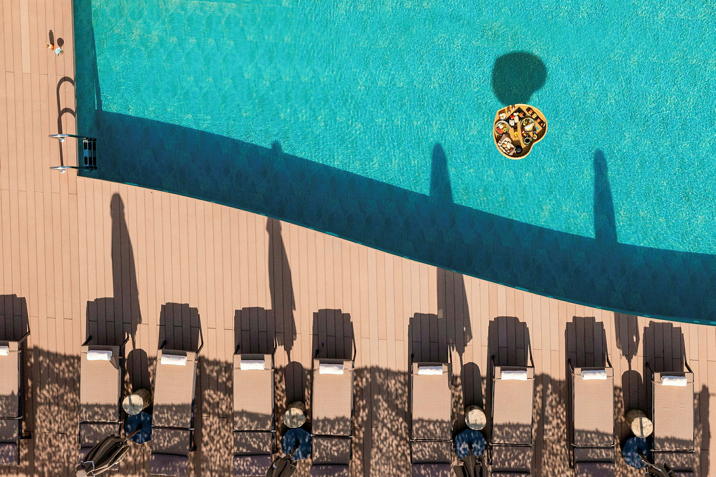 Flytande bricka med mat i en pool, solstolar på terrass bredvid. (AI-genererad text)