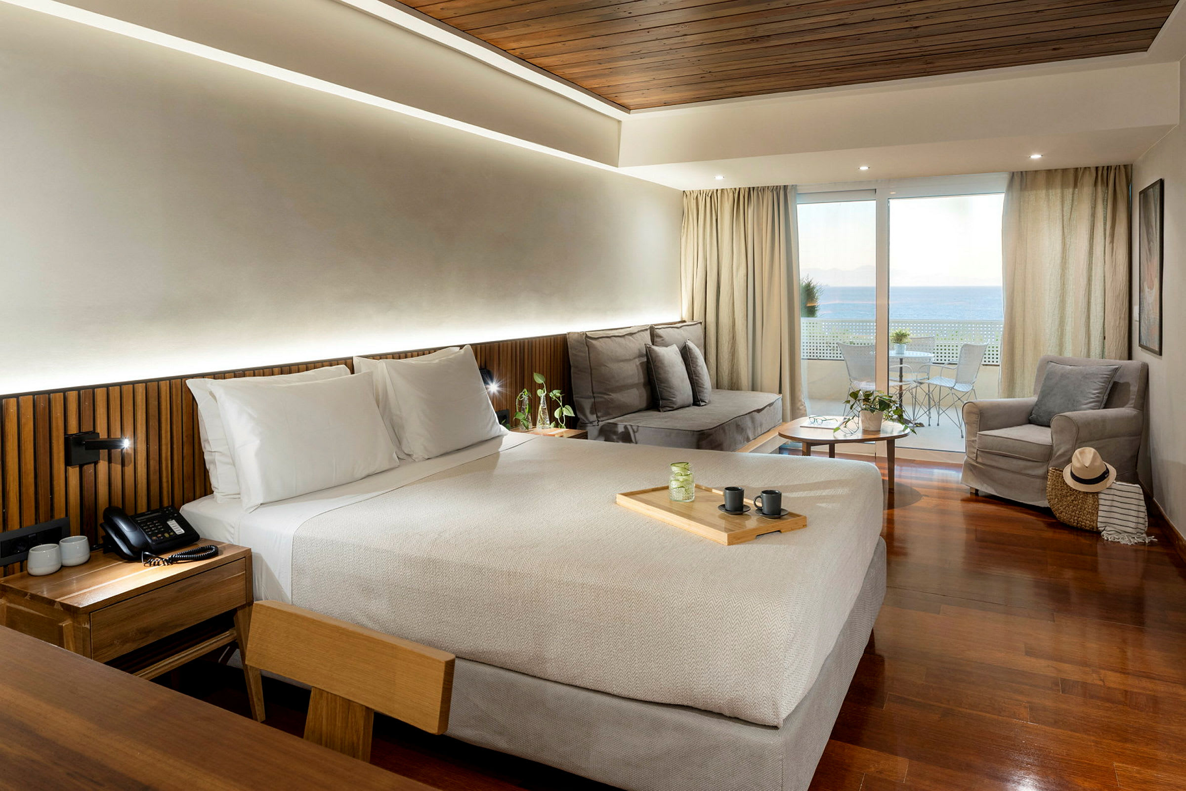 Ett hotellrum med en dubbelsäng, en sittgrupp med soffa och fåtölj, samt en balkong med utsikt över havet. (AI-genererad text)