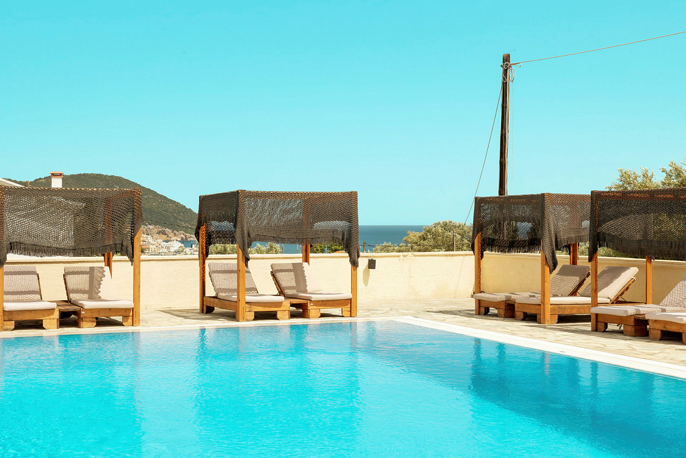 Bild av en pool med solstolar och skuggande tak i förgrunden, havet och landskapet synliga i bakgrunden. (AI-genererad text)