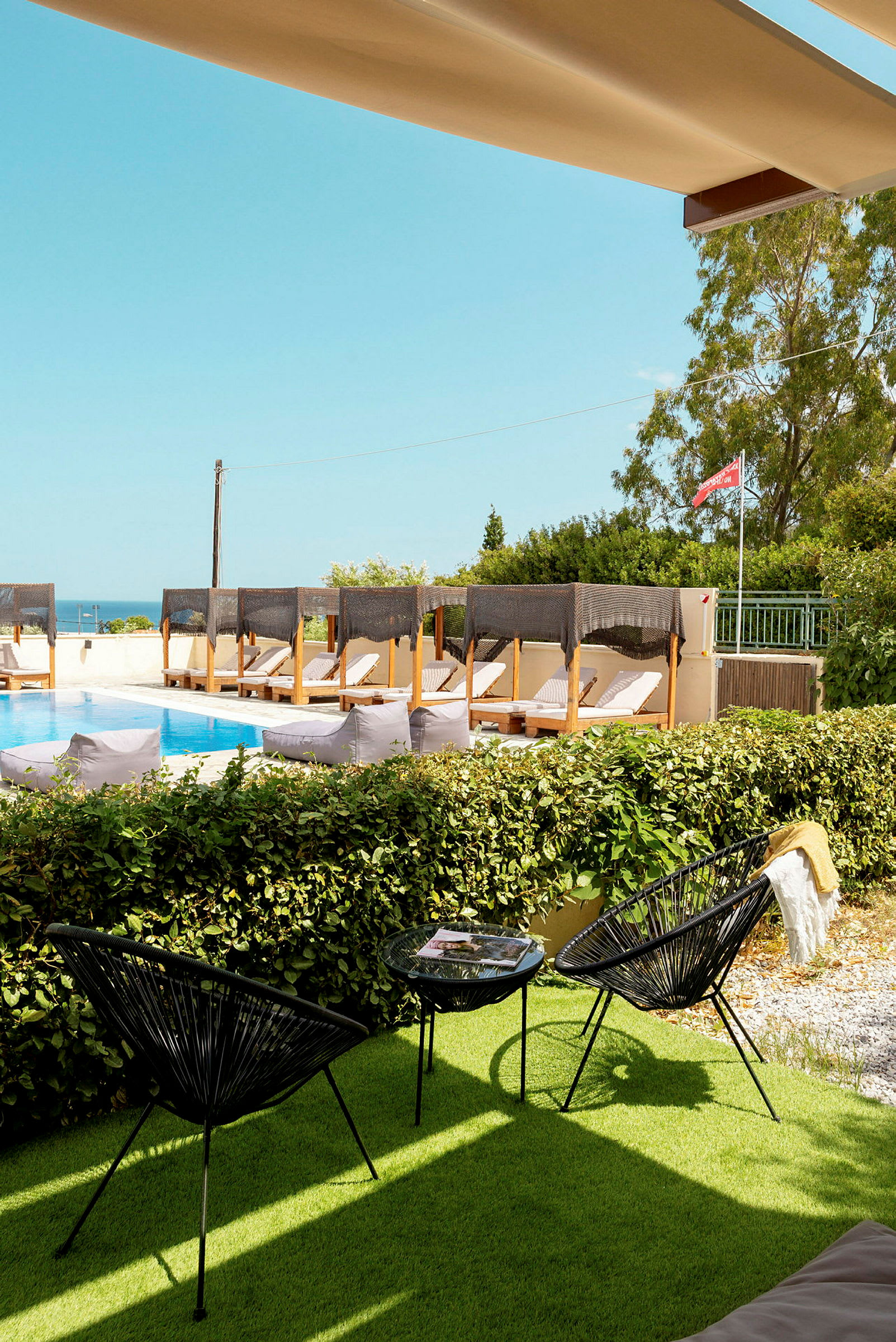 Bild av en pool med solstolar under baldakiner, några svarta stolar och ett bord på gräsmattan, i bakgrunden skylt med flagga. (AI-genererad text)