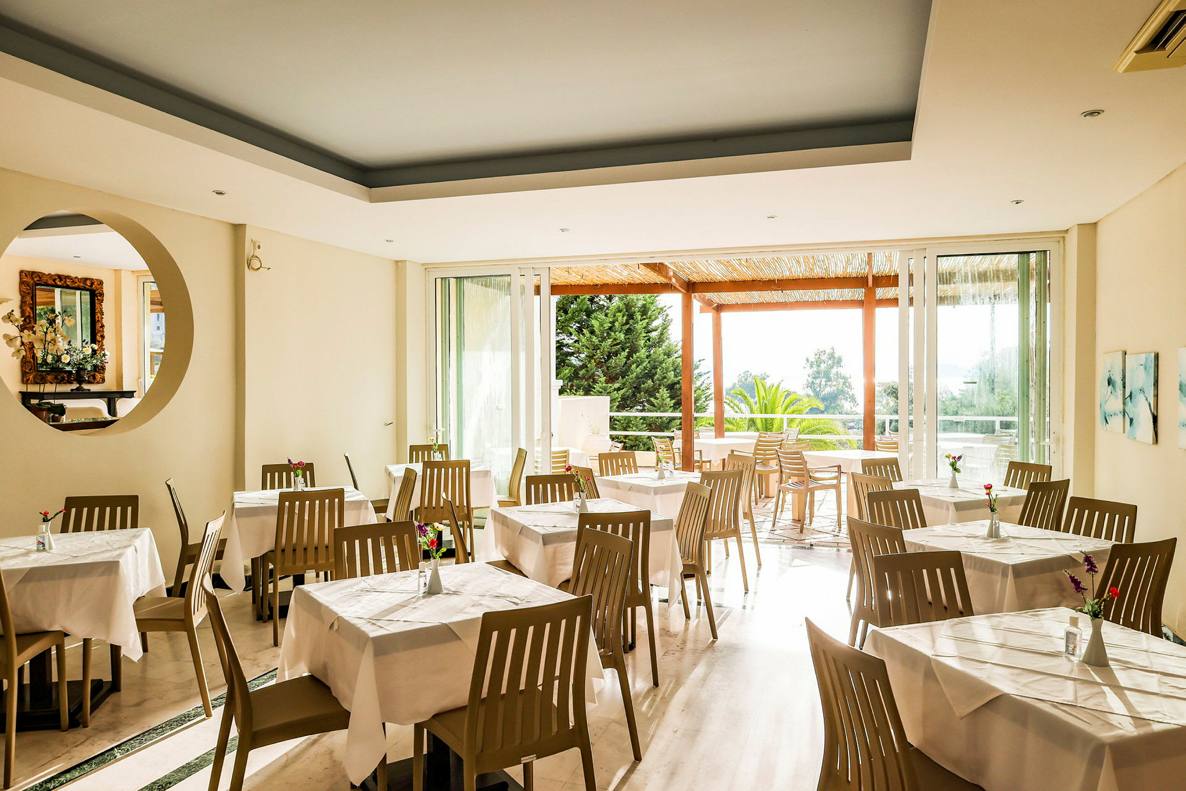 Restaurang med vita dukar och bruna stolar, ljusa väggar och utsikt mot en trädgårdsveranda. (AI-genererad text)