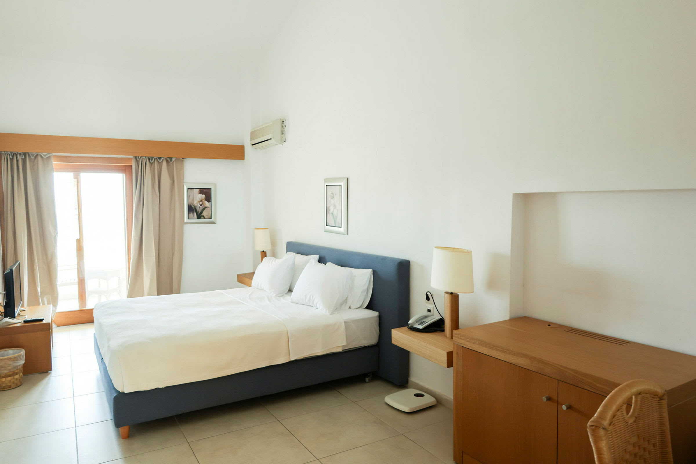 Ett hotellrum med en dubbelsäng, skrivbord och balkongdörr. (AI-genererad text)