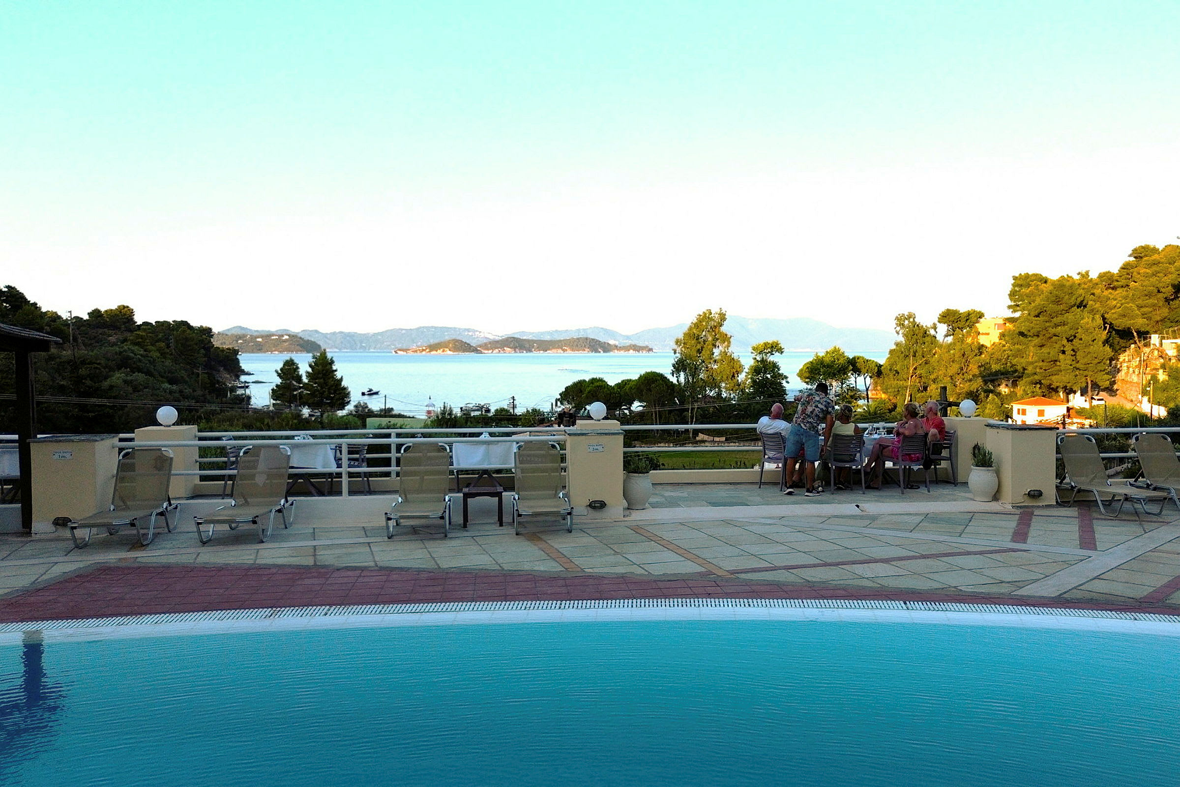 Utsikt från en poolterrass med solstolar, med hav och öar i bakgrunden. (AI-genererad text)