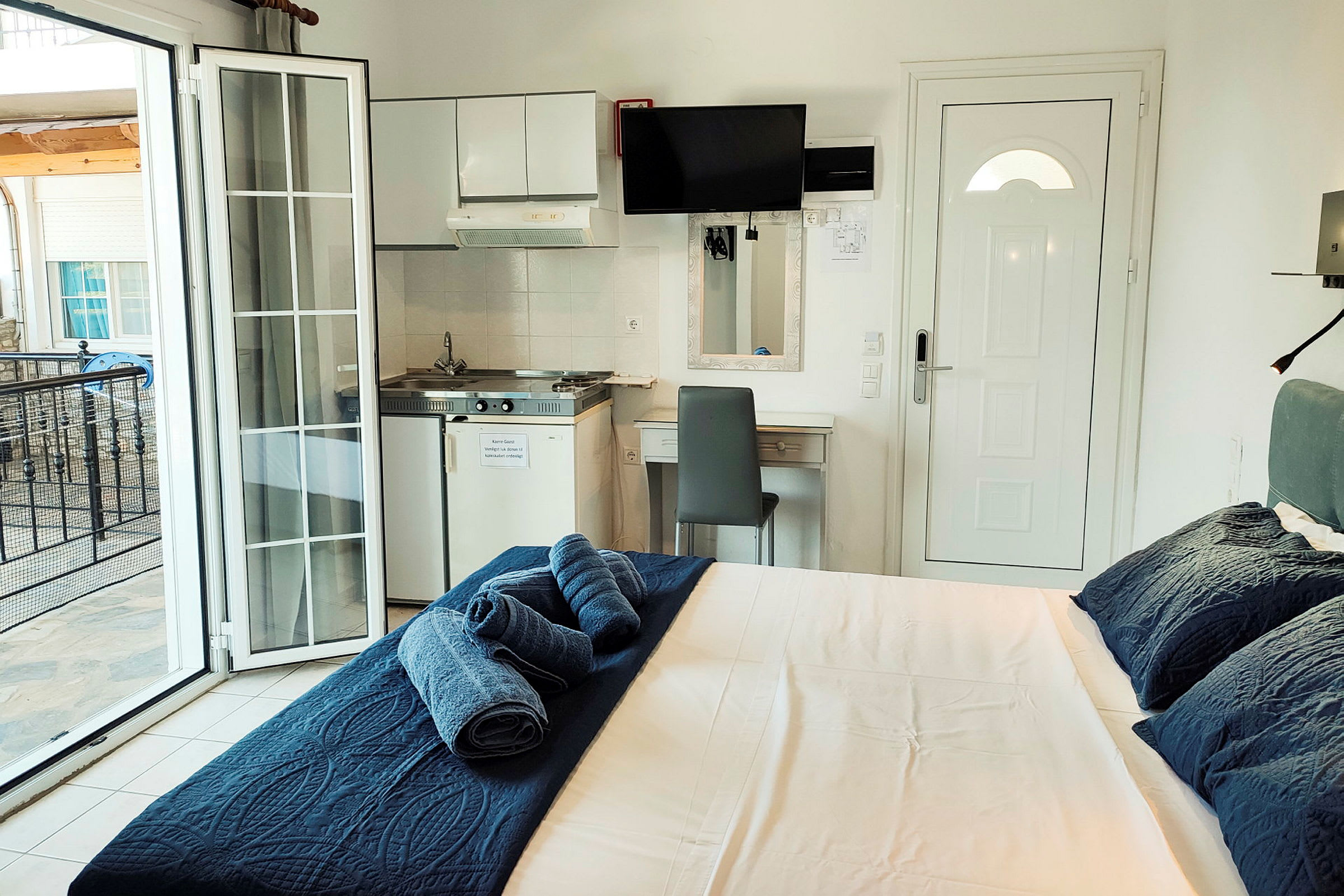 Ett hotellrum med en säng, en liten köksdel och en balkong. (AI-genererad text)